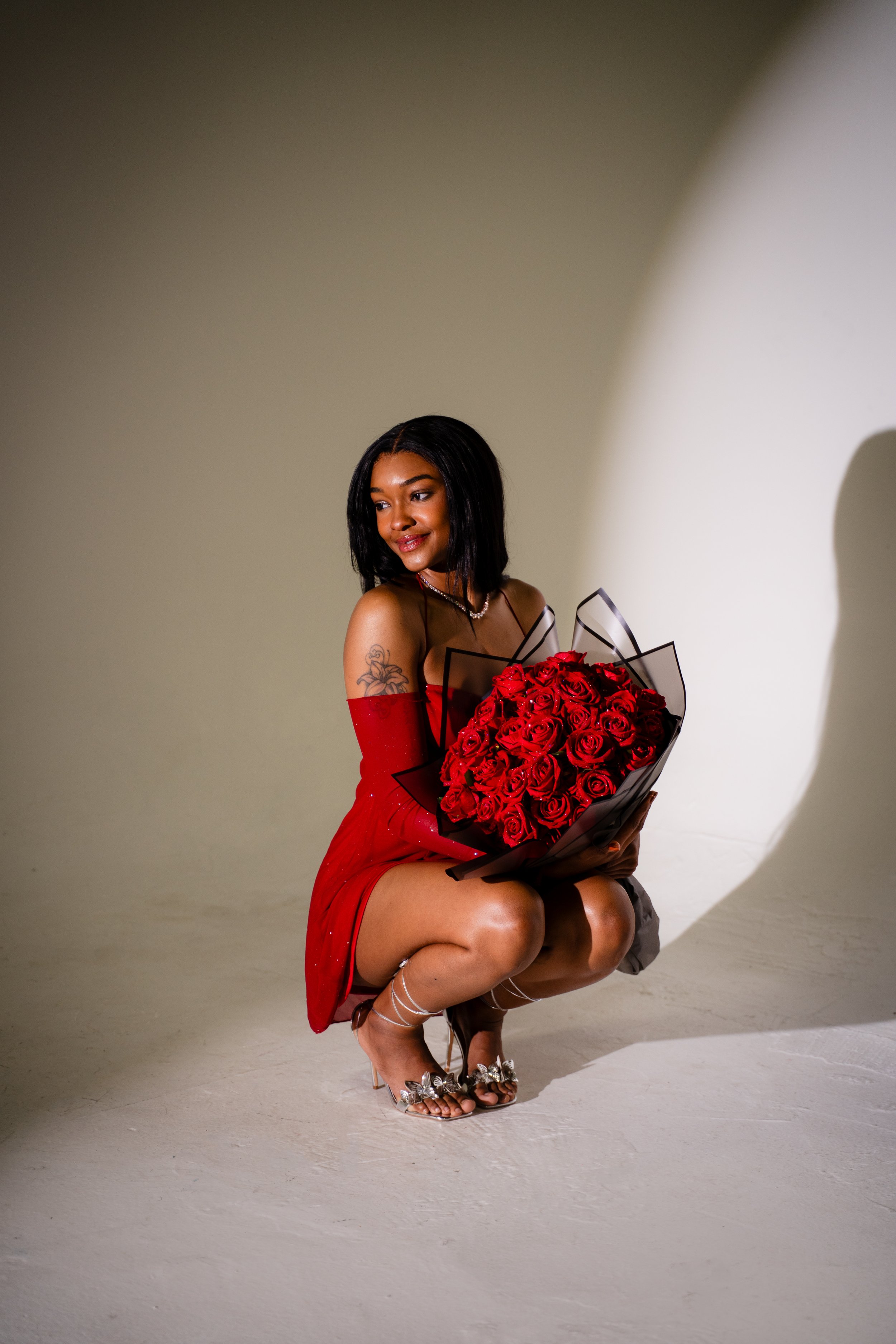 Woman in a red dress crouching with a bouquet of red roses.
