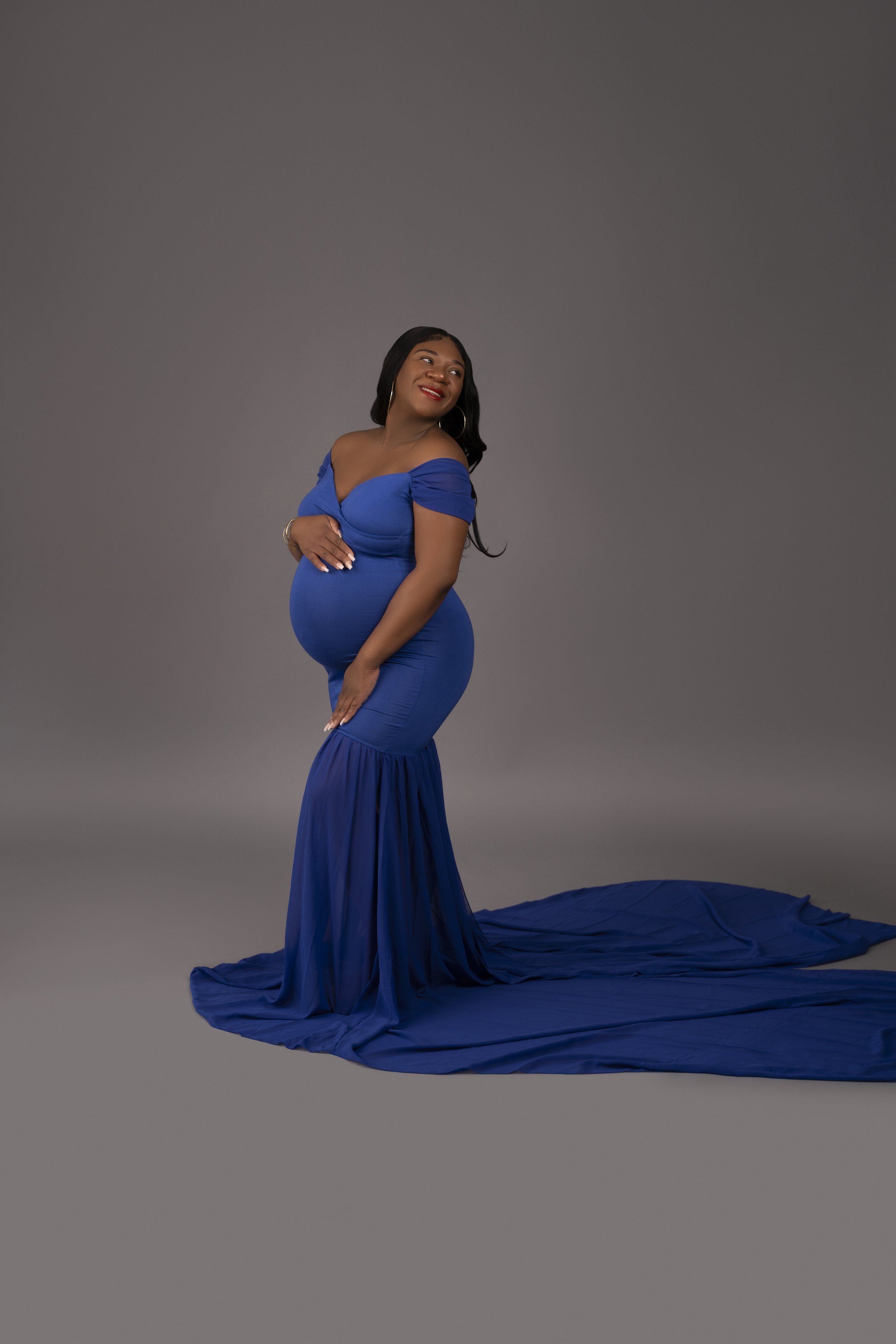 Pregnant woman in a blue gown posing against a gray background
