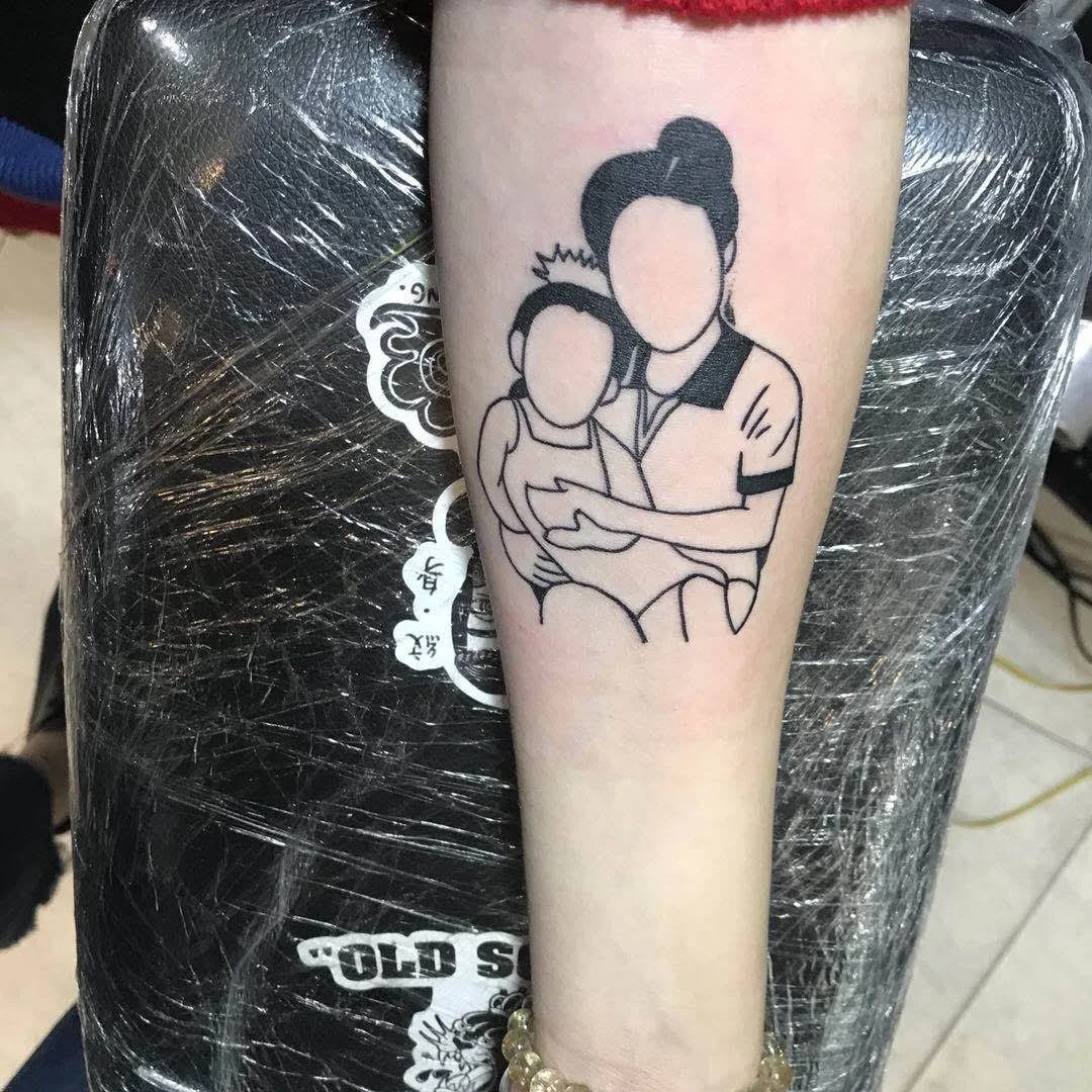 Tattoo of a faceless line art depicting a person with a bun holding a child wearing a crown on an arm.