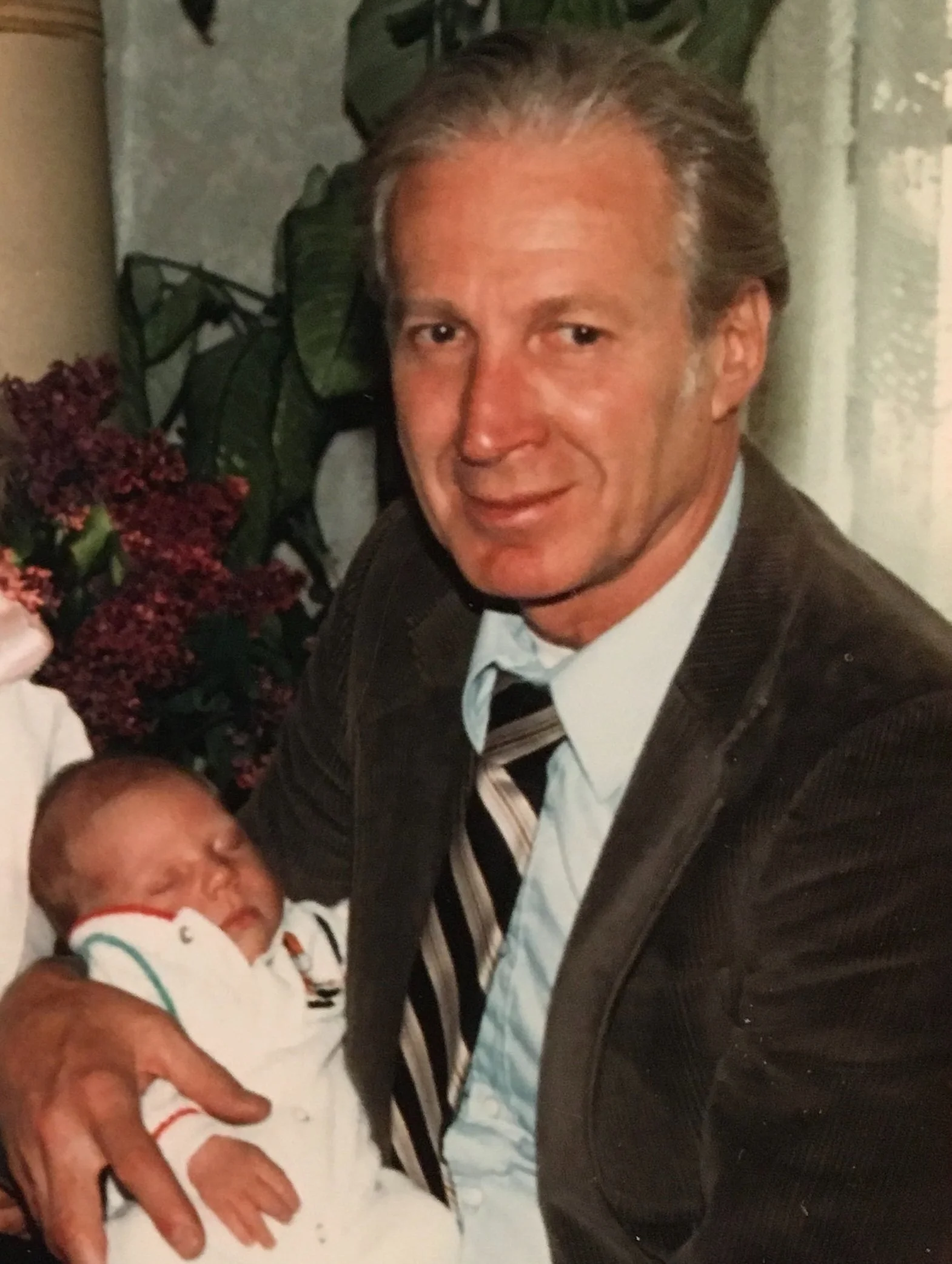 A middle-aged man in a suit and tie holding a sleeping newborn baby.