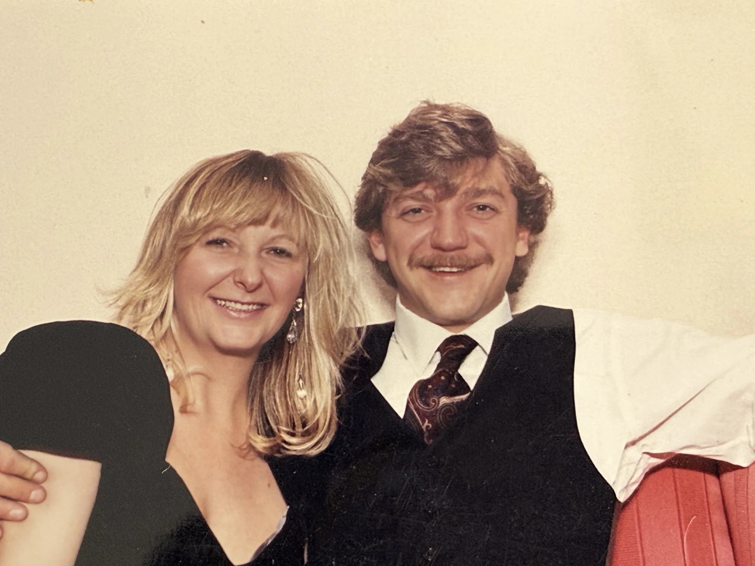 A man and woman sitting close together, smiling at the camera, in a vintage style photo.