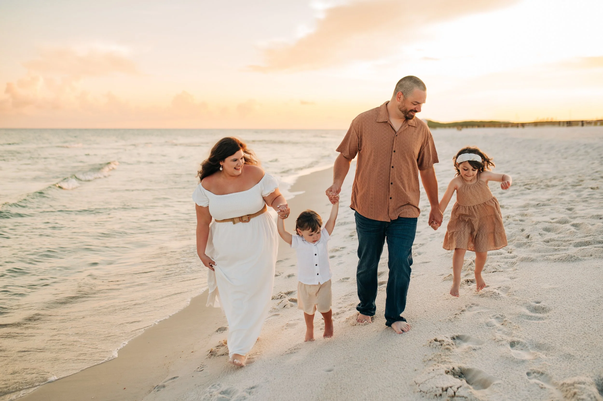 Family of four walking on the beach at sunset, holding hands and smiling.