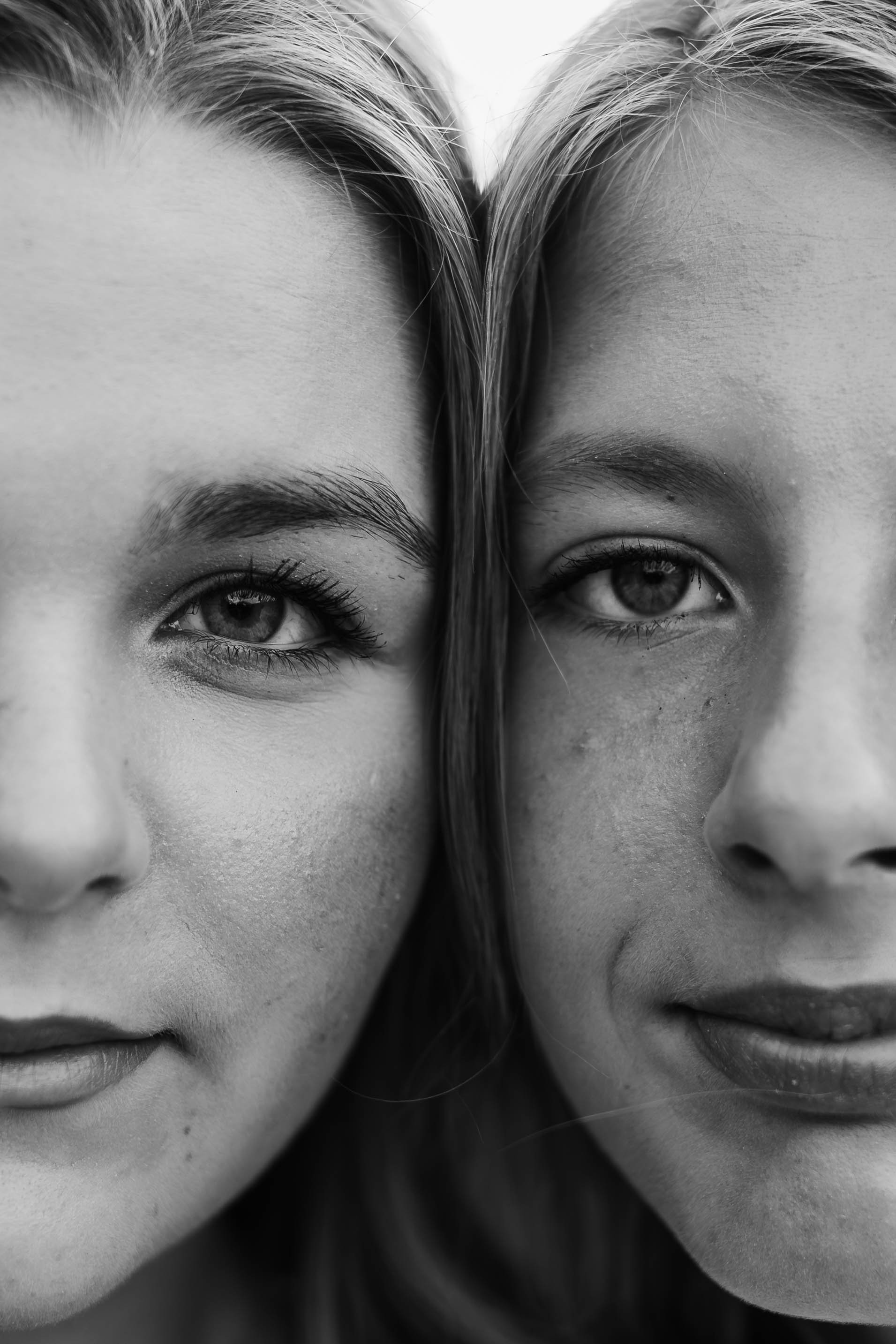 Close-up black and white photo of two young women with their faces touching, focusing on their eyes and noses.