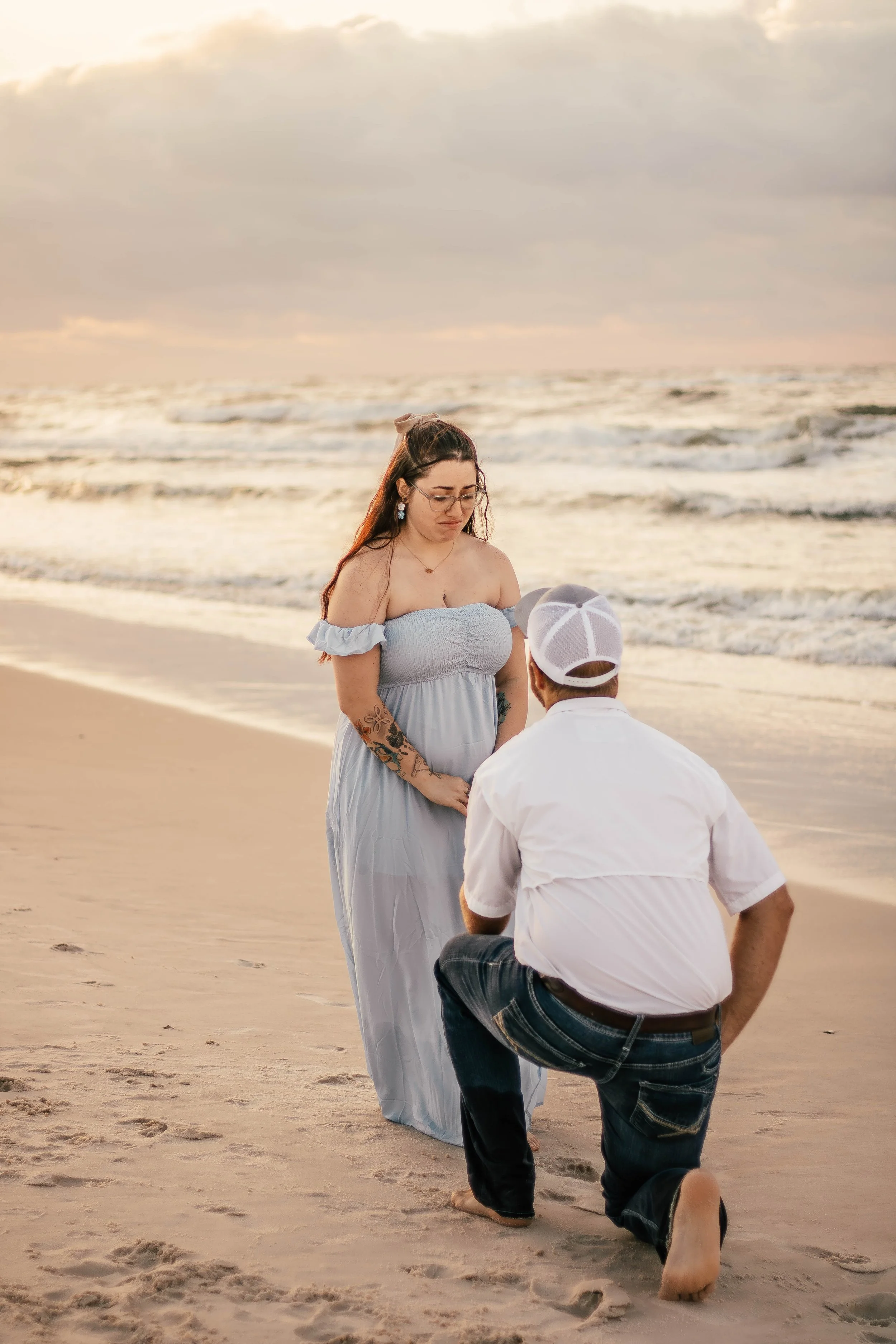 A man proposes marriage to a pregnant woman on the beach during sunset.