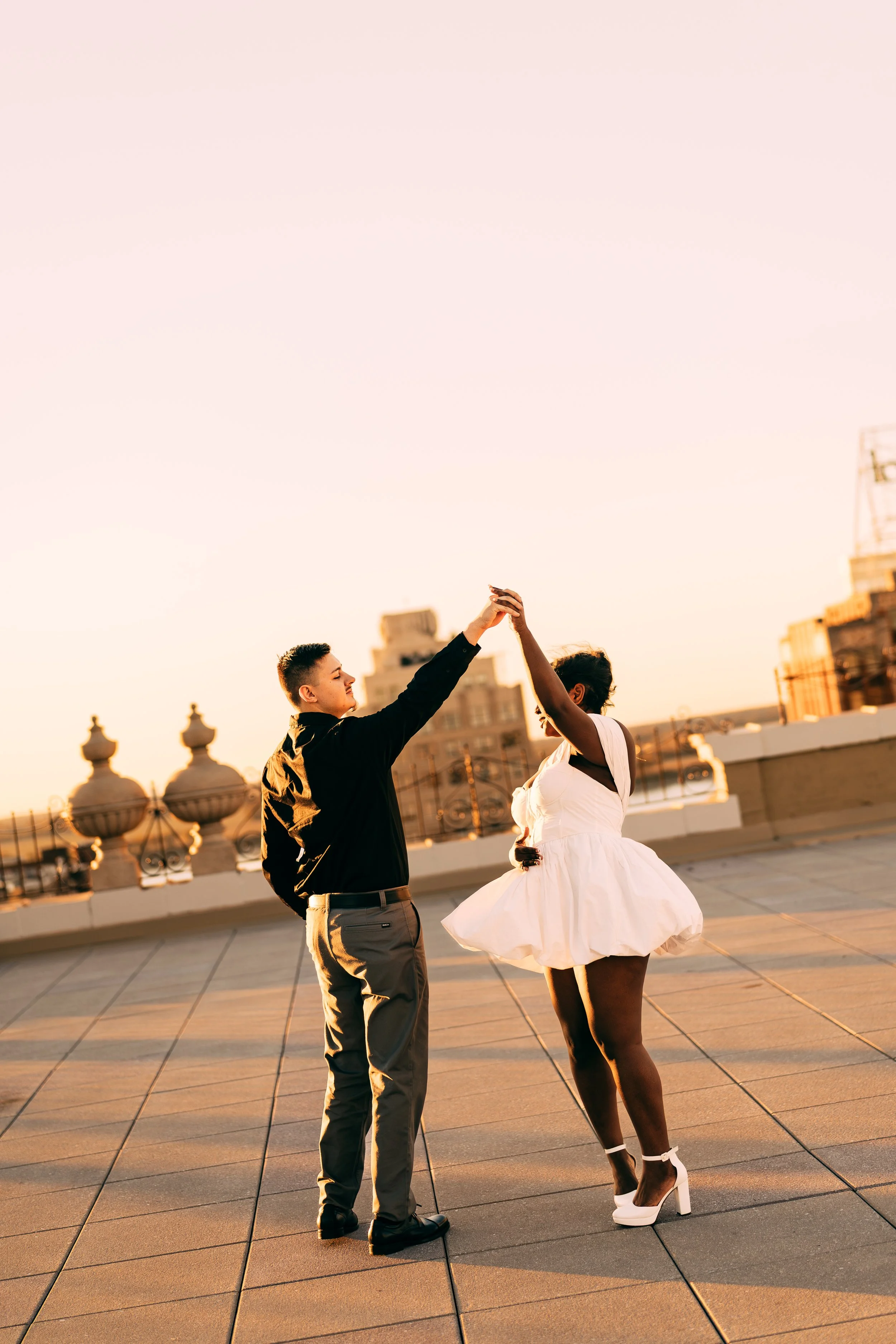 A couple dancing on a rooftop at sunset, with city buildings in the background.