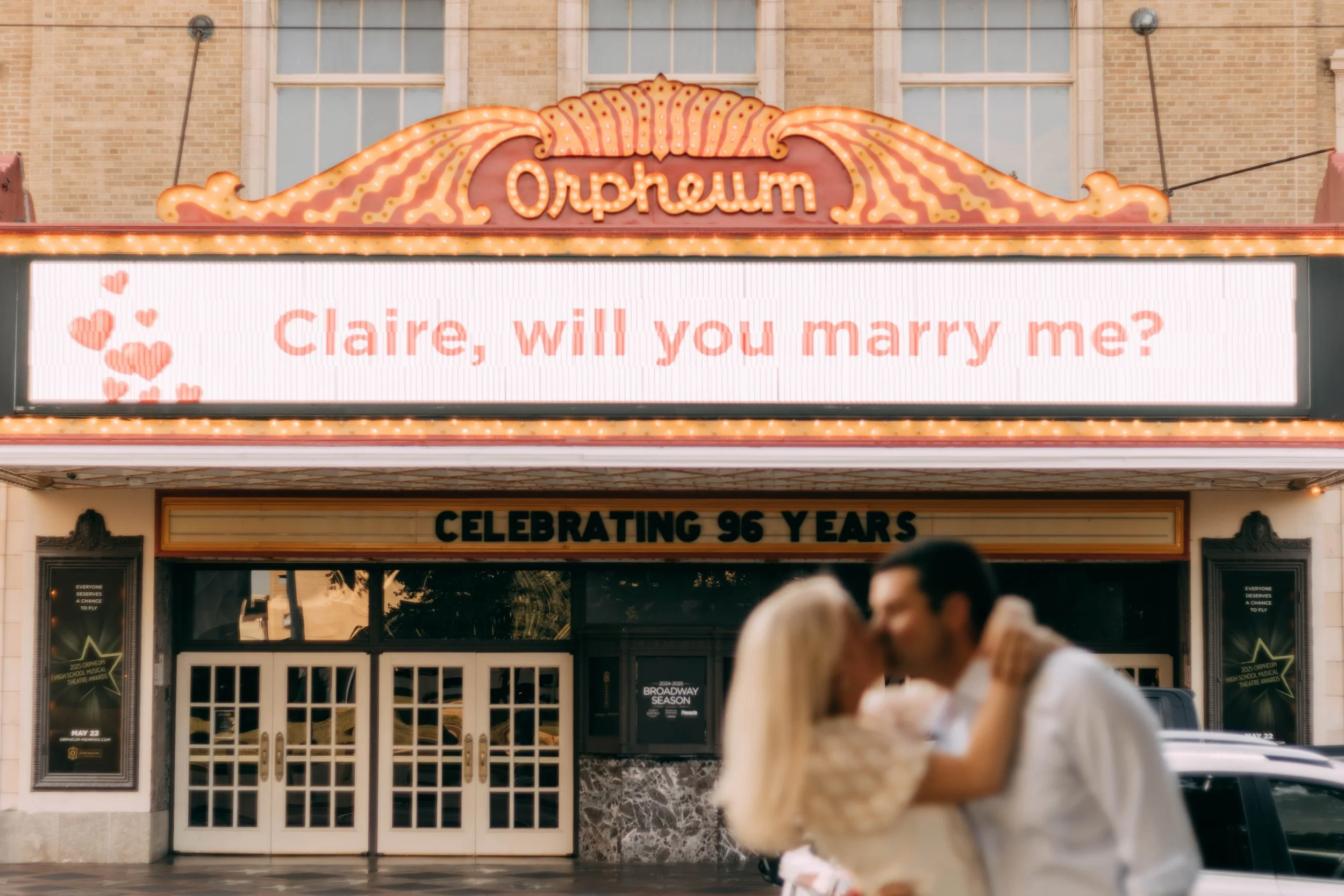 A couple kissing in front of the Orpheum theater, which has a marquee reading, 'Claire, will you marry me?' The theater is celebrating 96 years.