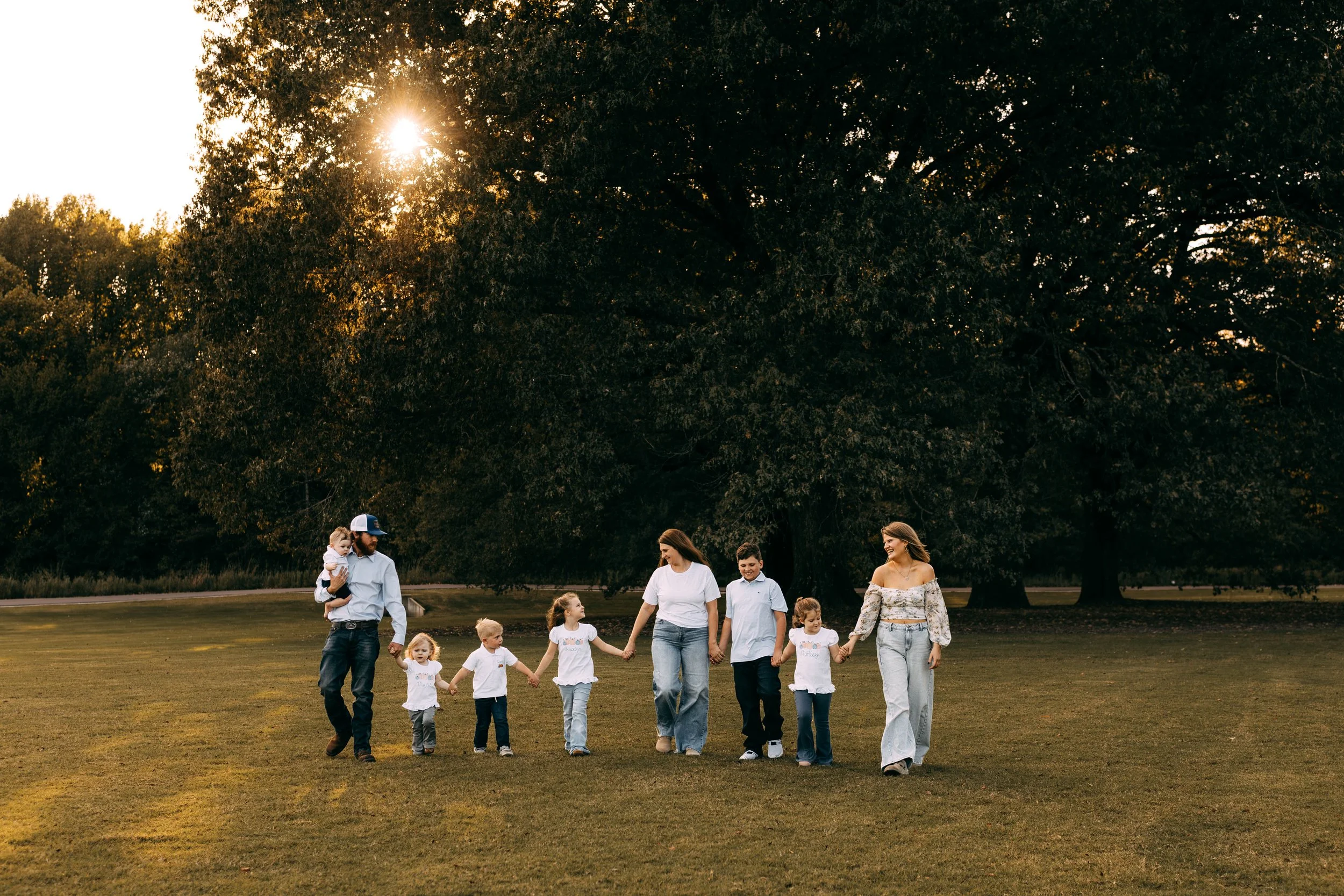 Family walking hand in hand outdoors in a park during sunset.