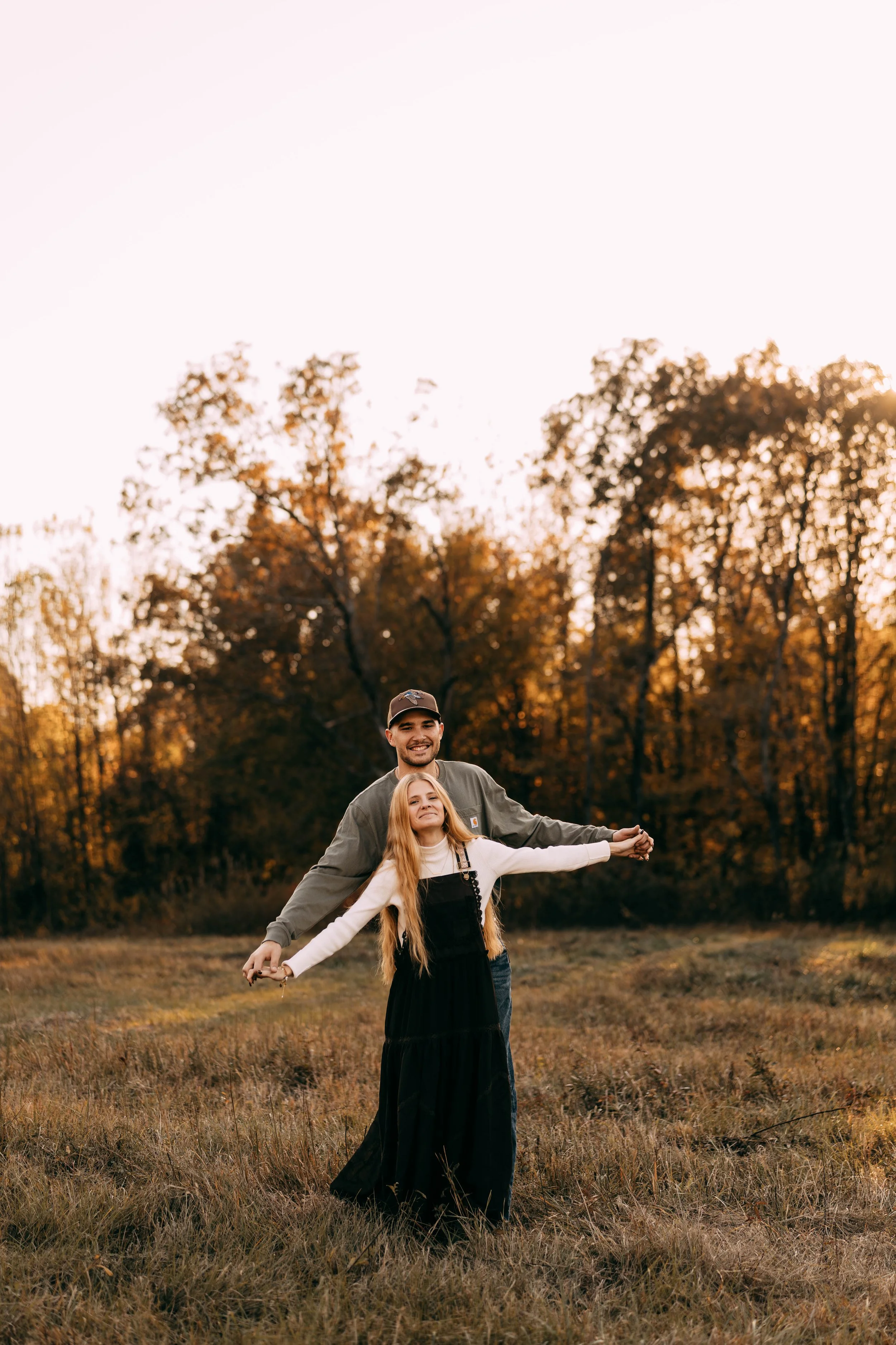 A man and a girl holding hands in a field with trees in the background during sunset.