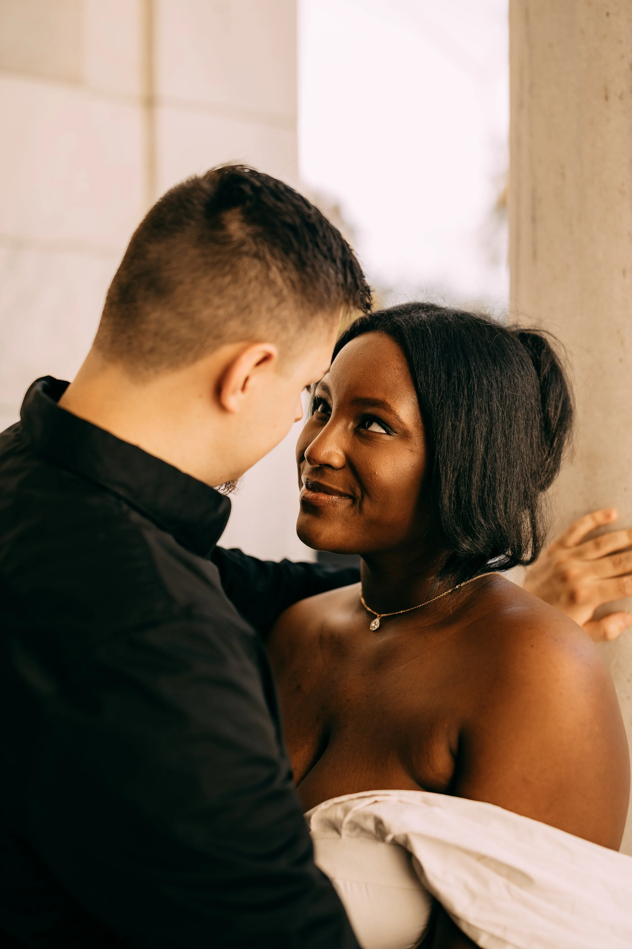 A couple sharing an intimate moment, standing close with faces inches apart, in a warm setting.