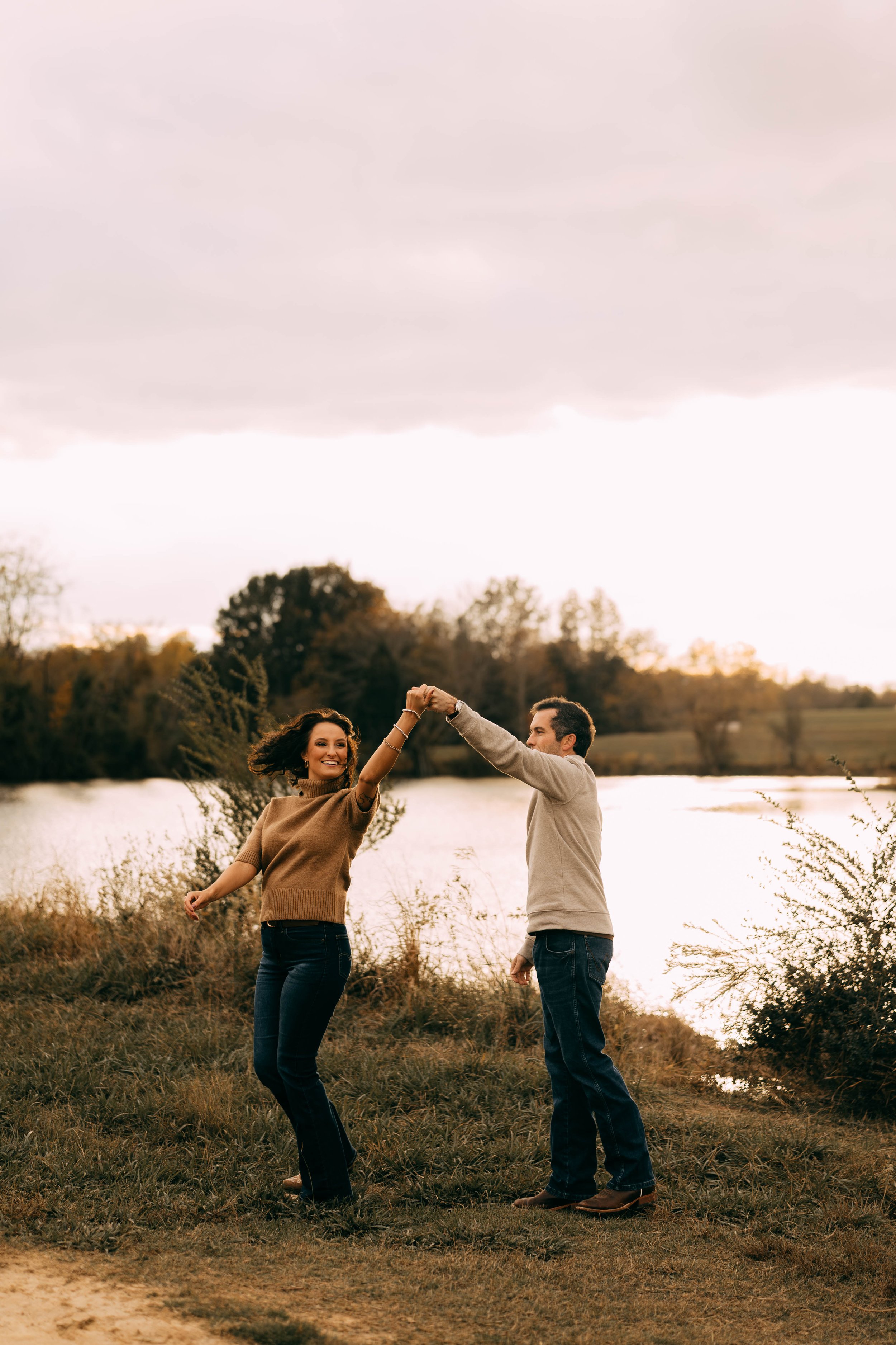 A couple dancing and enjoying themselves by a lake on a cloudy autumn day.