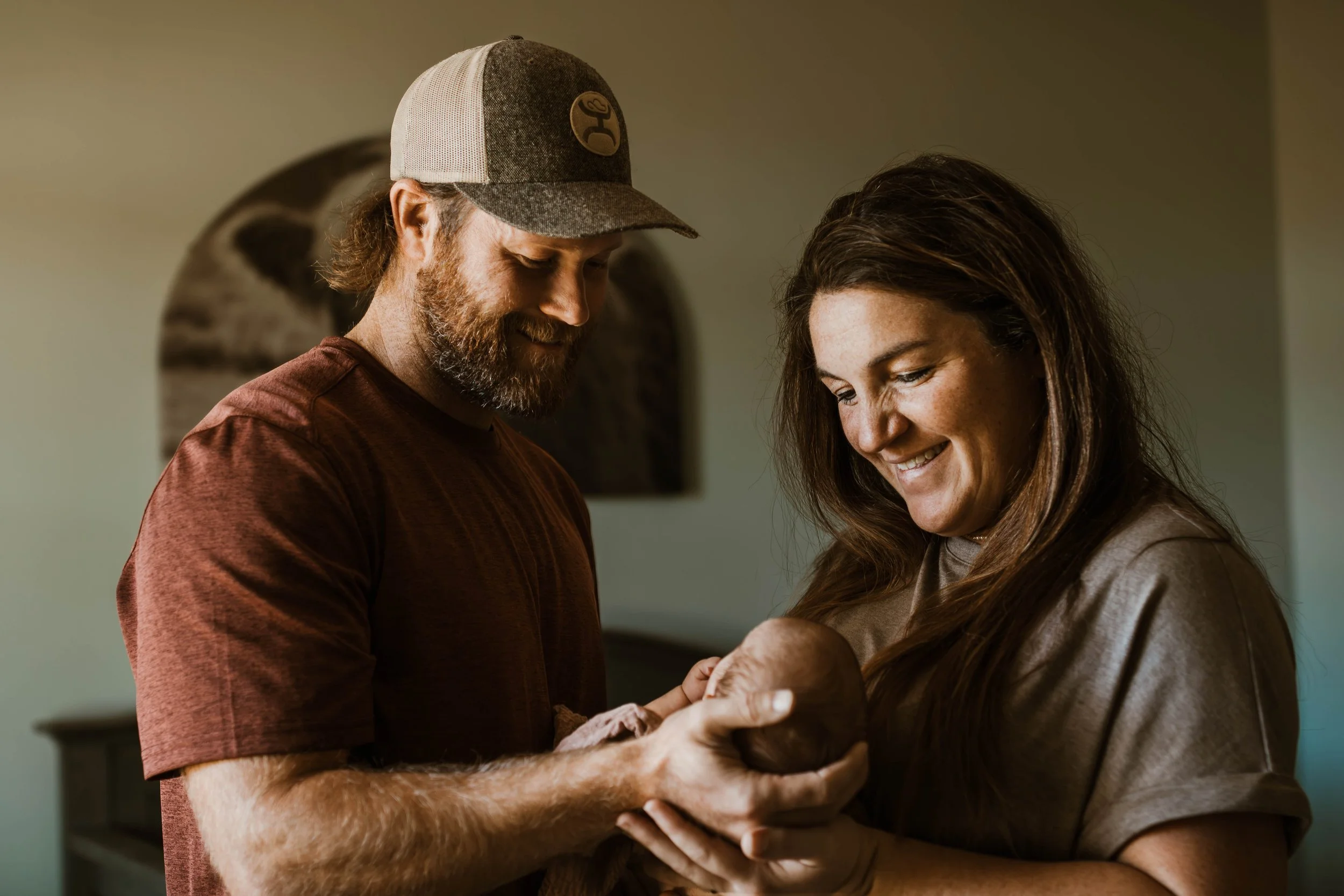 A man and woman look joyfully at a newborn baby they are holding together in a home setting.
