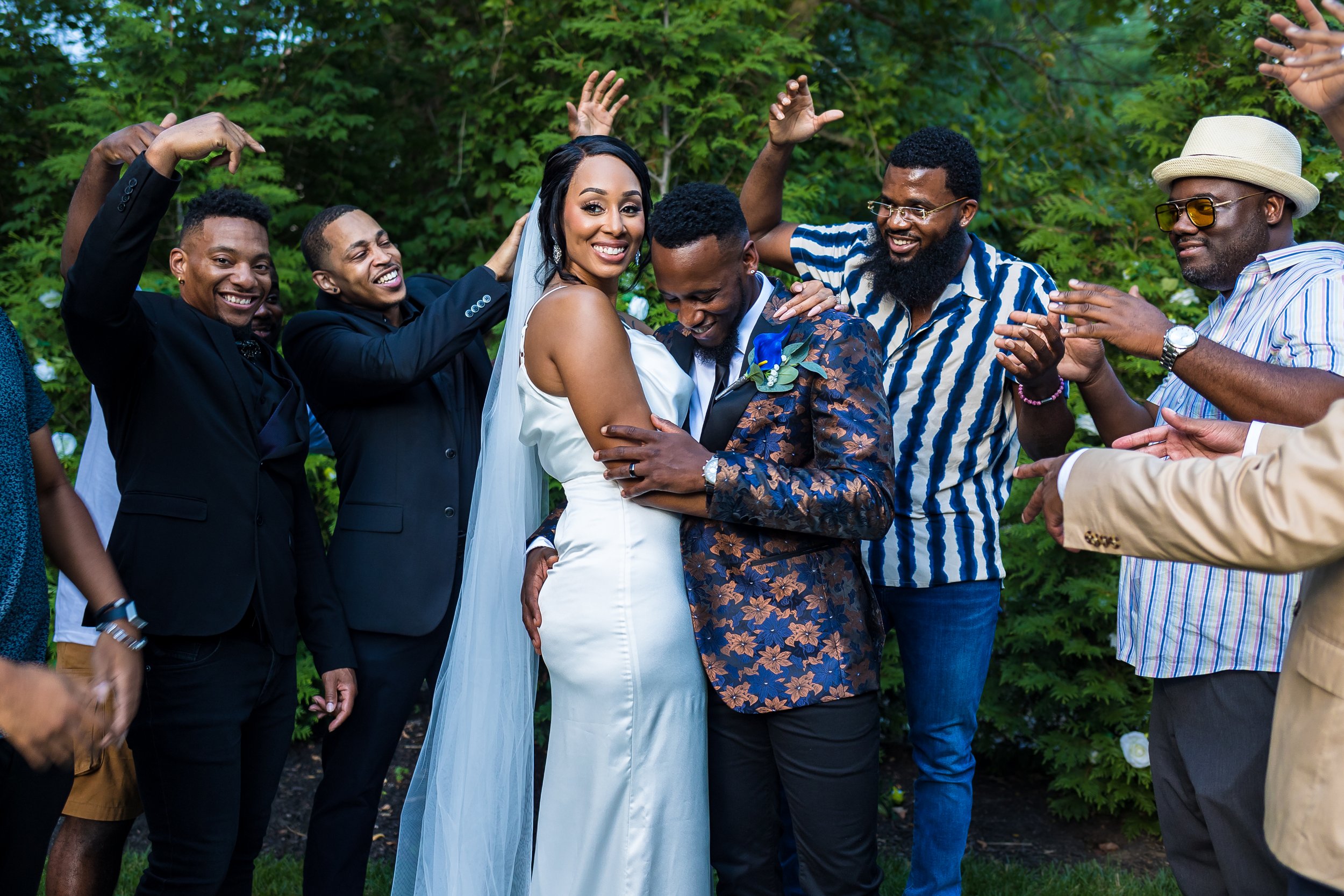 A bride and groom smiling and embracing each other surrounded by friends during a joyful outdoor wedding celebration.
