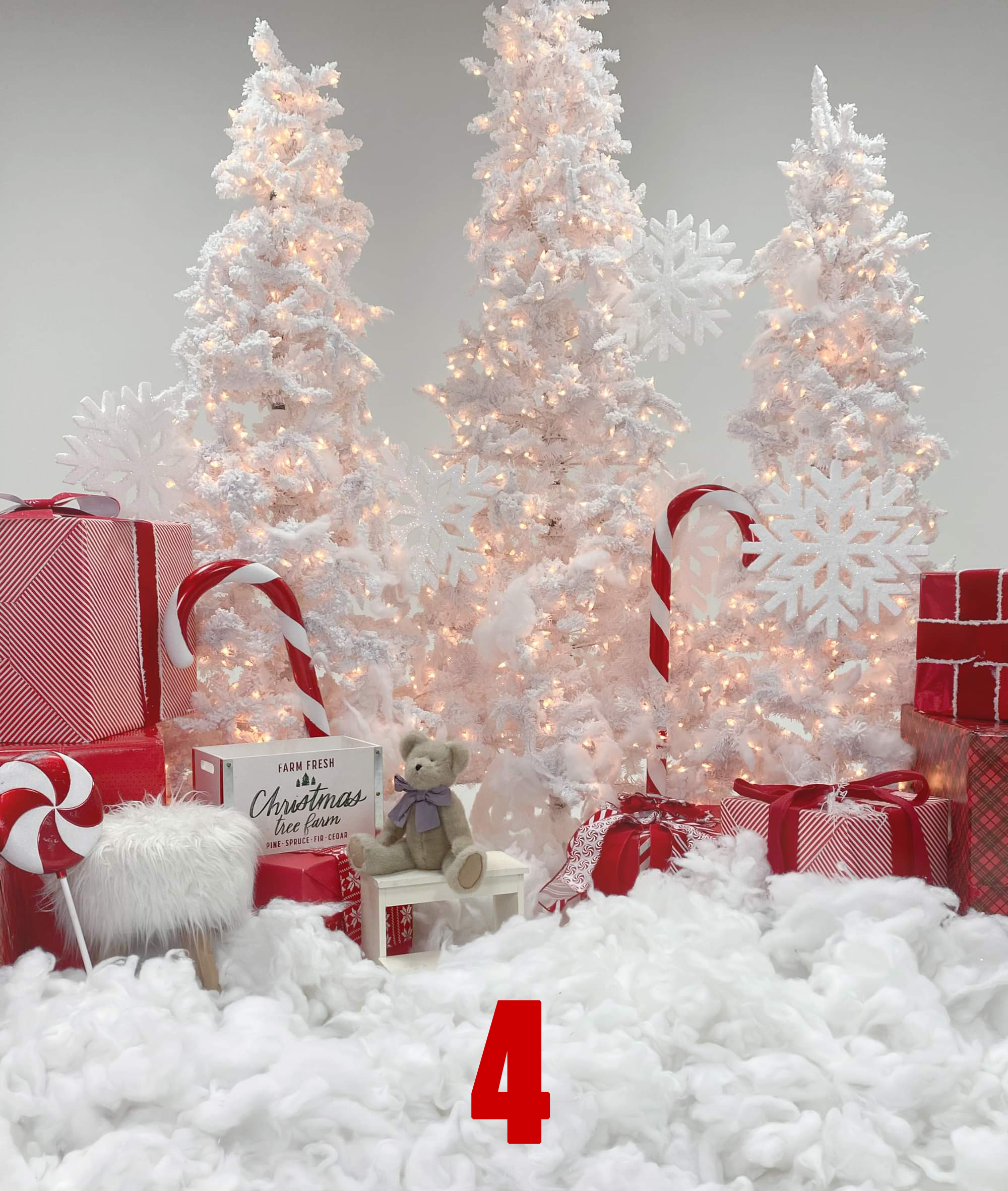 Decorative white Christmas scene with lit Christmas trees, red and white candy canes, red and white wrapped presents, a small white fur-covered stool, and a teddy bear with a purple bow, all set on a fluffy white surface.