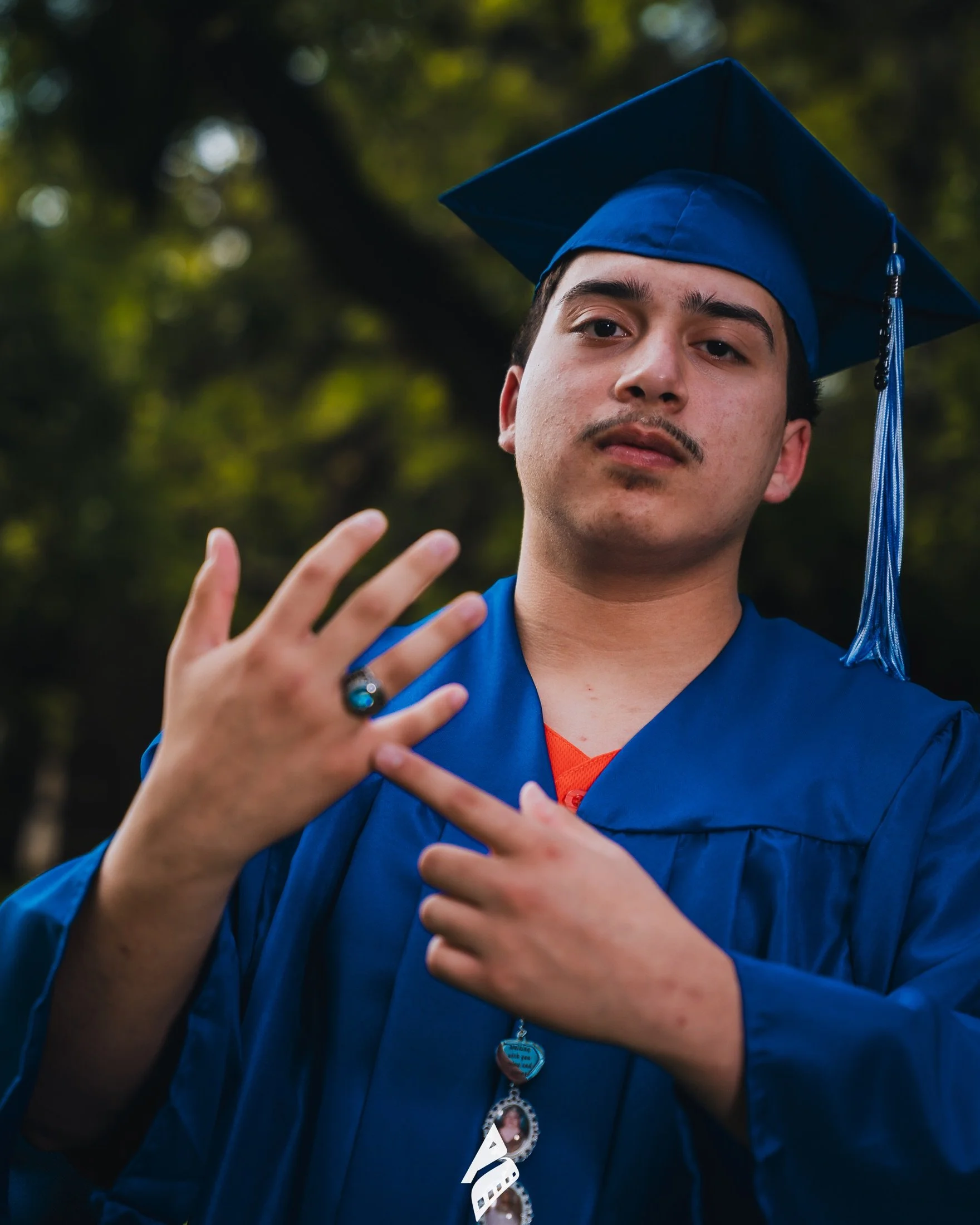 Graduate in blue cap and gown showing his class ring.