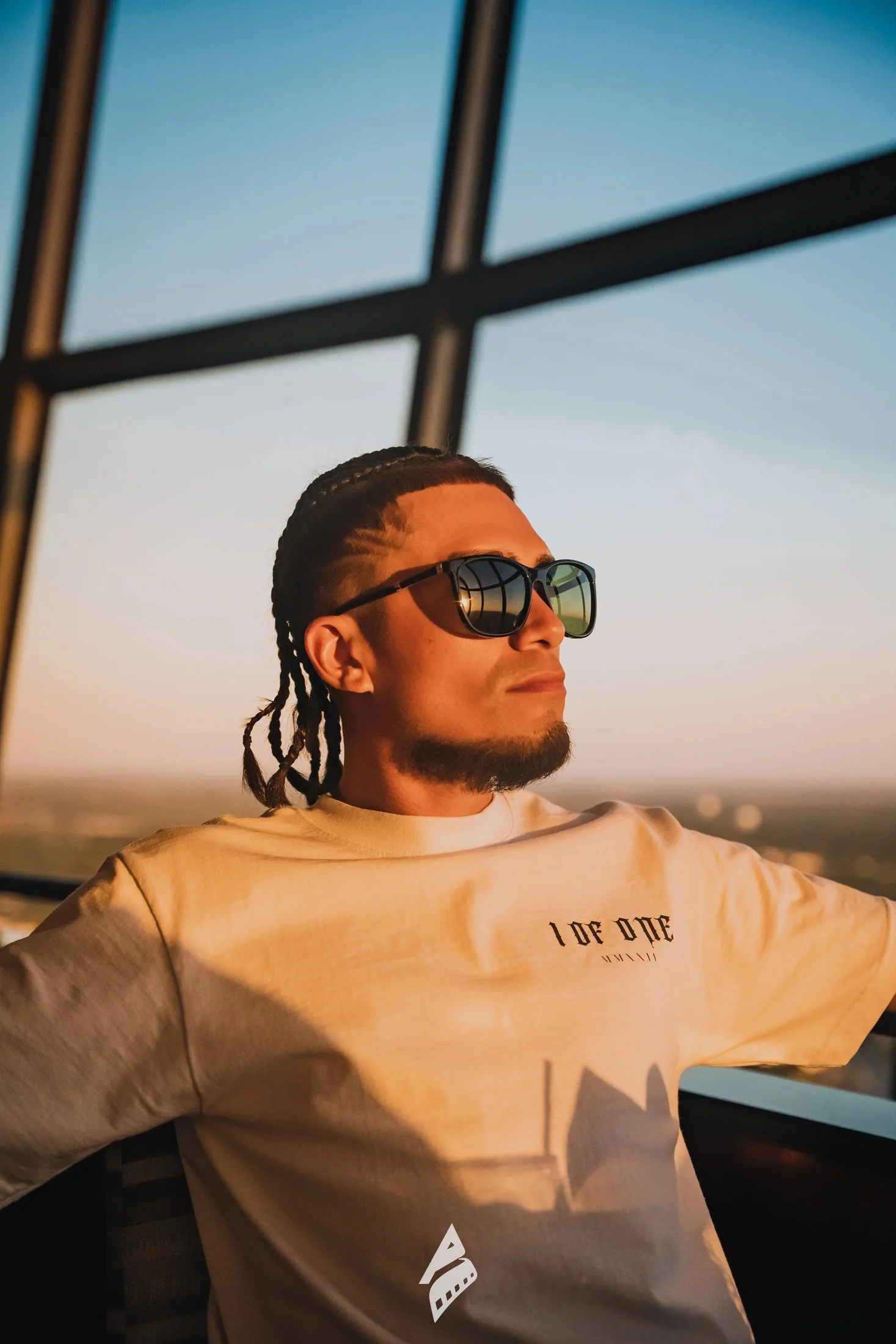 Man wearing sunglasses and a beige shirt in warm window light.