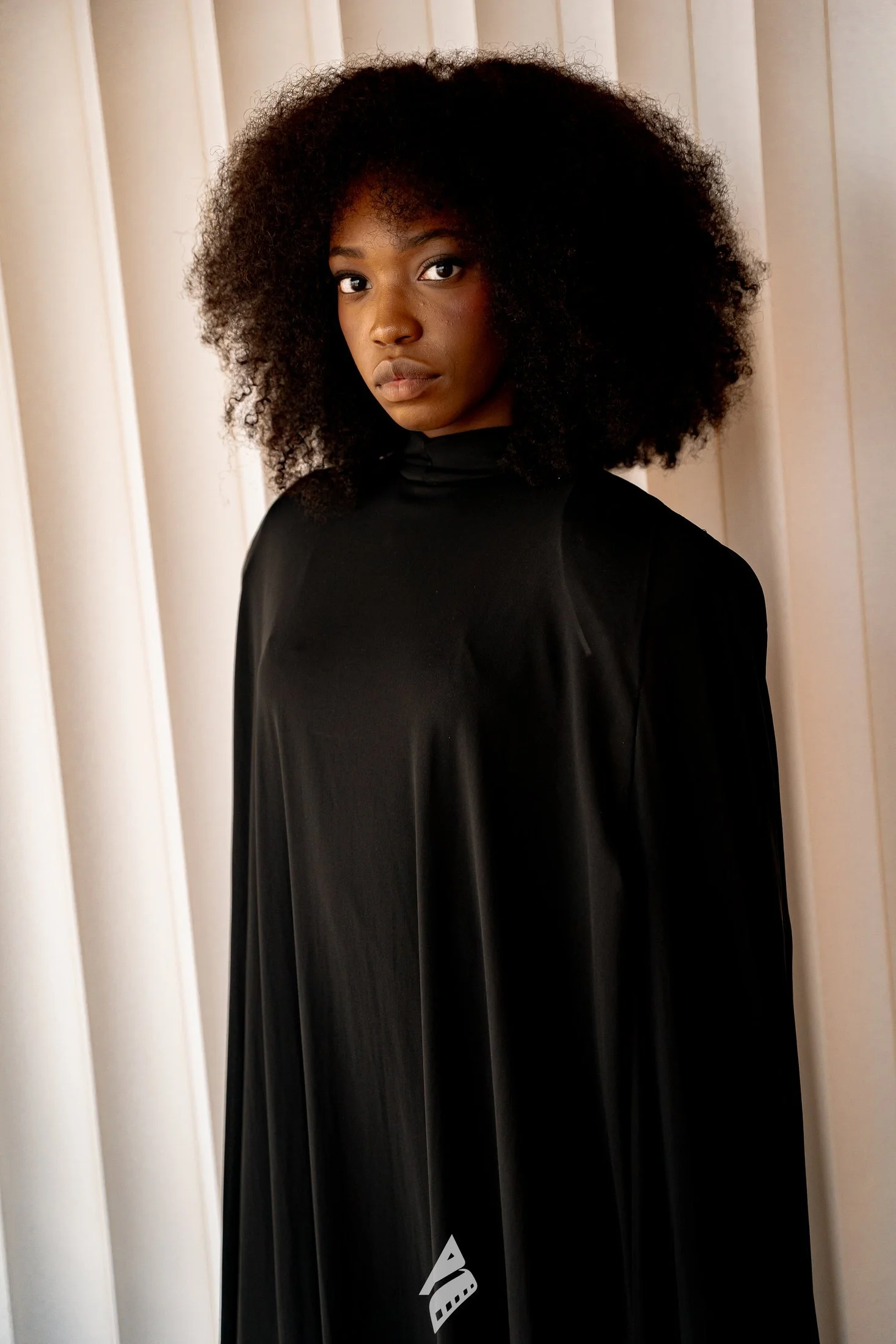 Woman in a black dress against a white curtain backdrop.