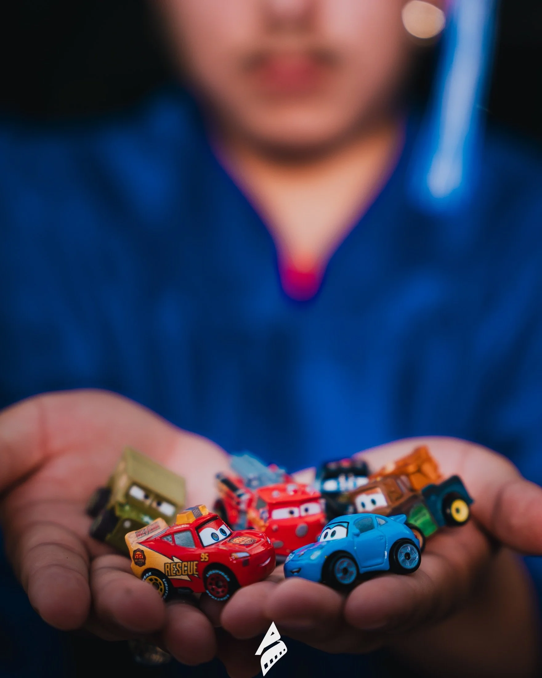 Toy cars held in the graduate’s hands, with his blue gown in the background.