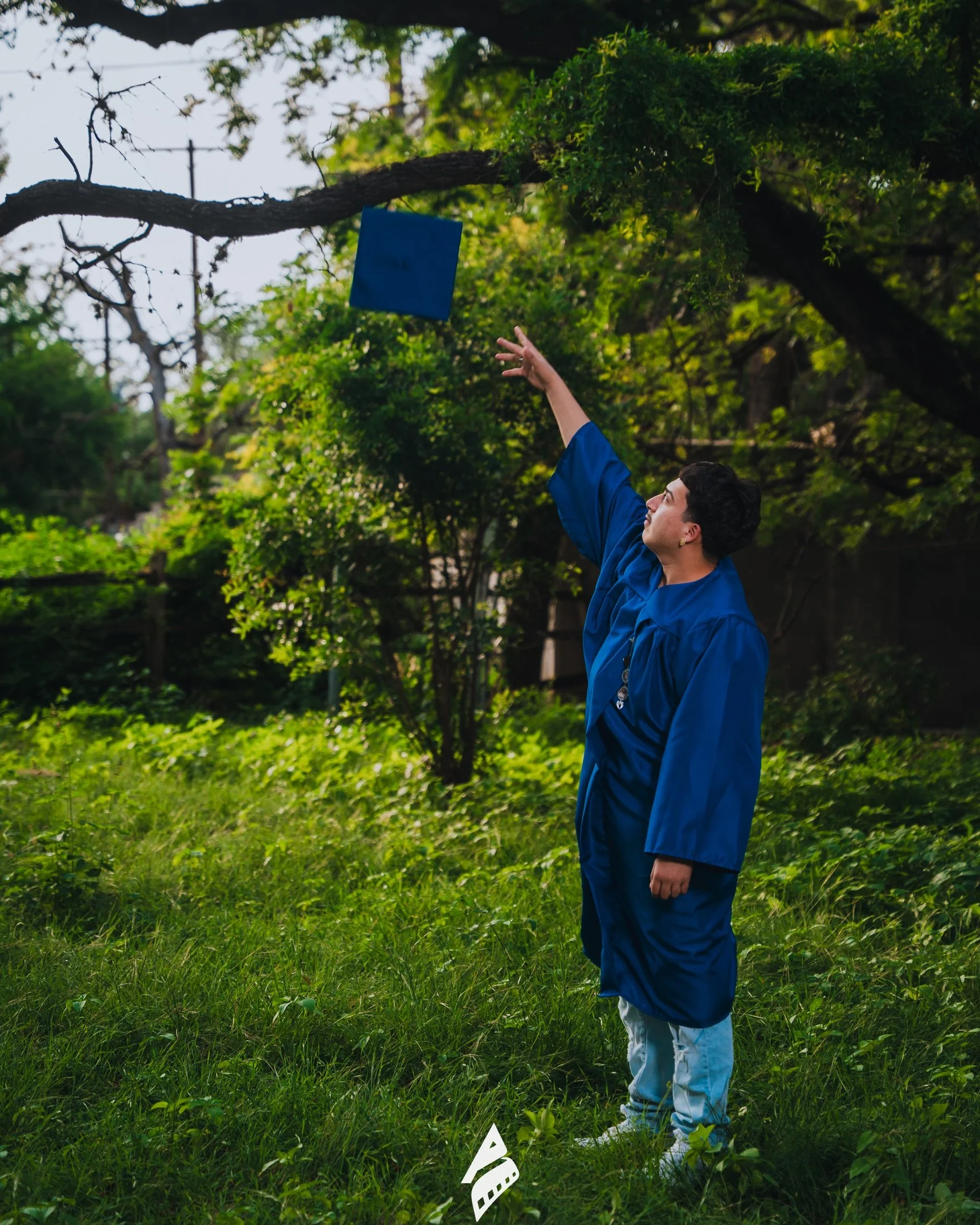 Graduate tossing his blue cap beneath the trees.