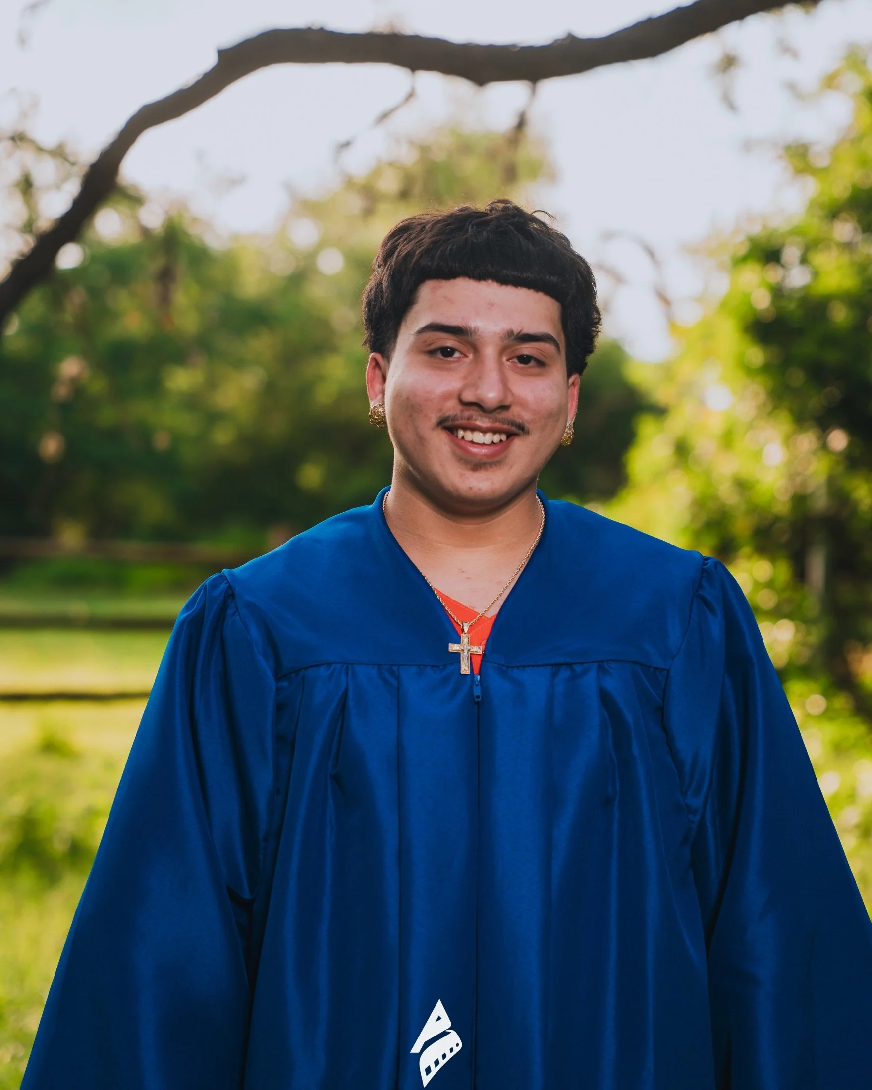 Smiling graduate in a blue gown during an outdoor senior portrait session by Antwan Productions
