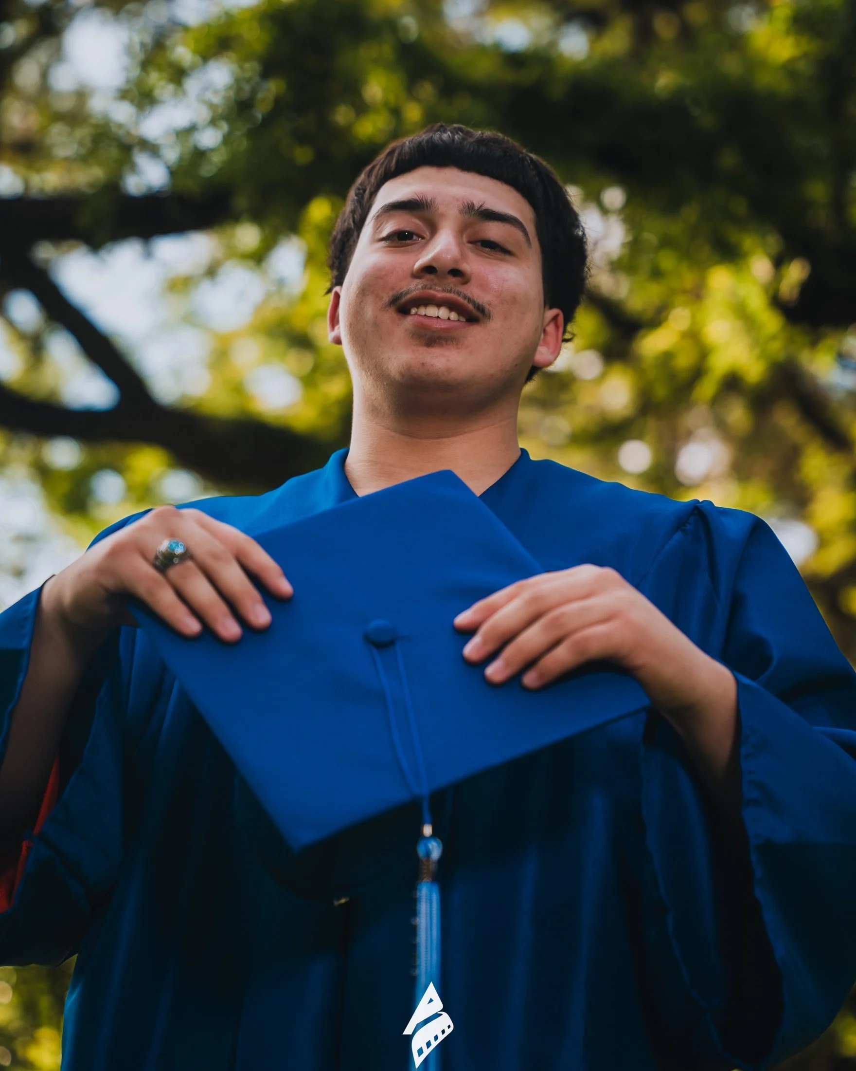 Smiling graduate holding his blue cap outdoors.