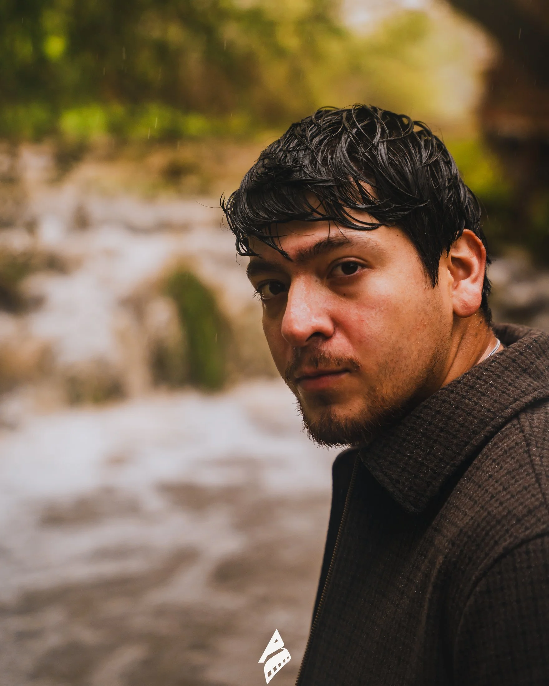 Close-up portrait of a man in a brown jacket beside flowing water.