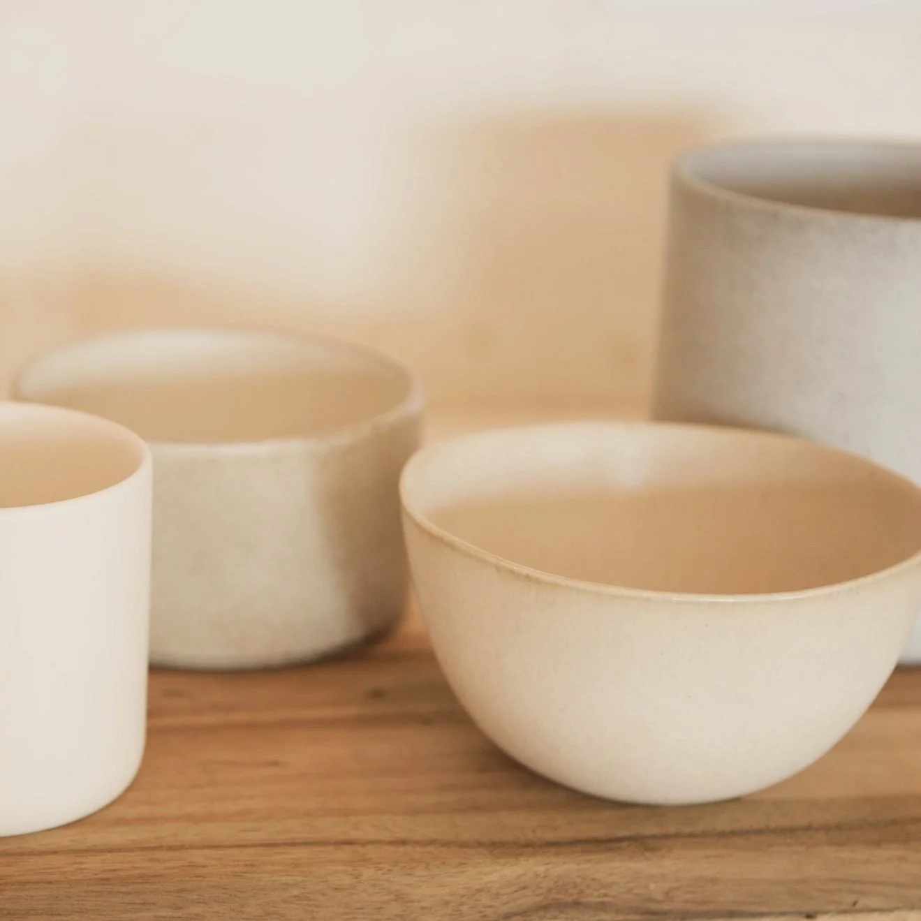 Four cream-colored ceramic bowls of varying sizes arranged on a wooden surface with a neutral background.