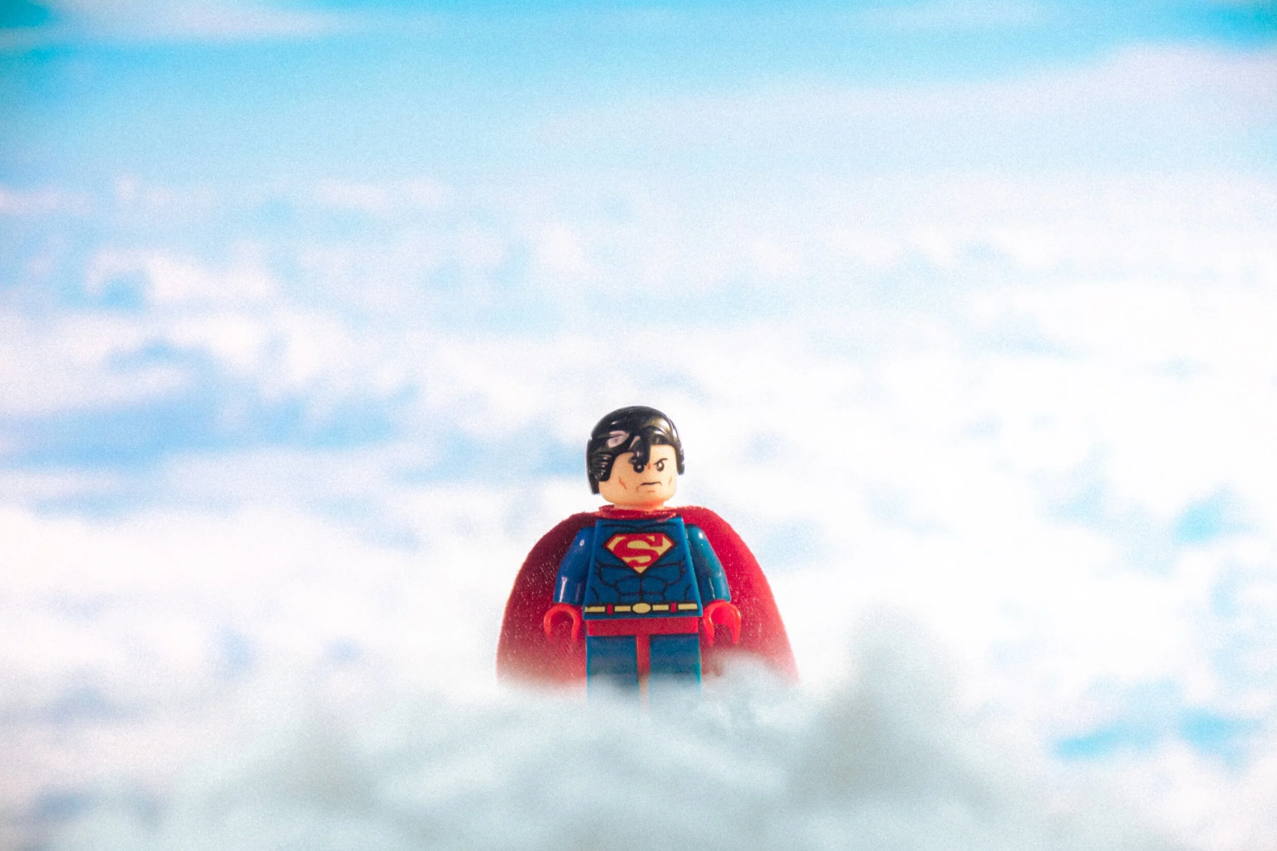 Lego Superman figure standing on clouds with blue sky background.