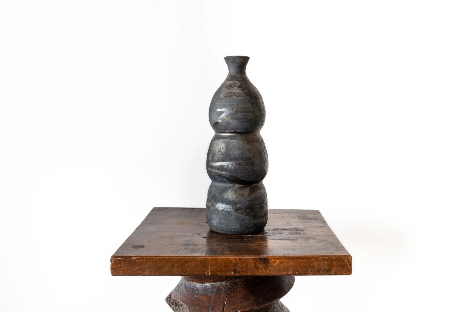 Vintage dark ceramic wabi-sabi vase displayed on a carved wooden pedestal against a white background.