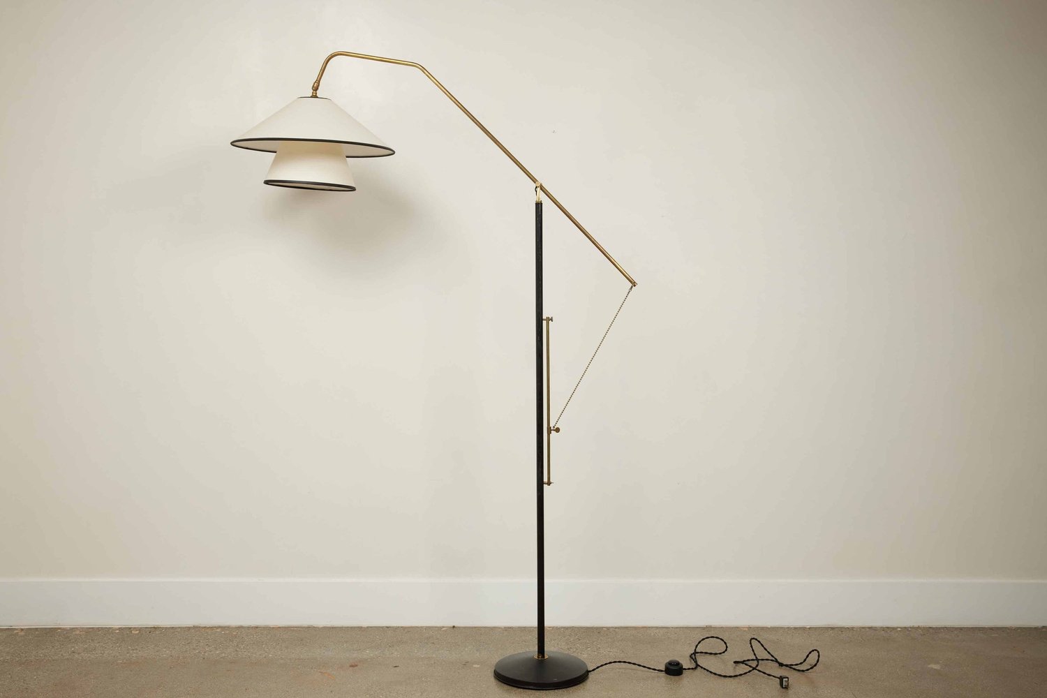 Vintage mid-century modern brass and black floor lamp with tiered shade against a white wall.