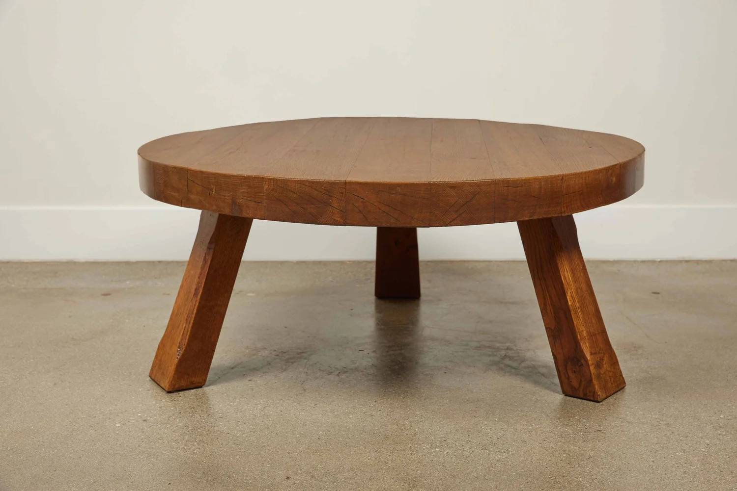 Vintage mid-century modern round wooden coffee table with thick top and angled legs on a concrete floor.