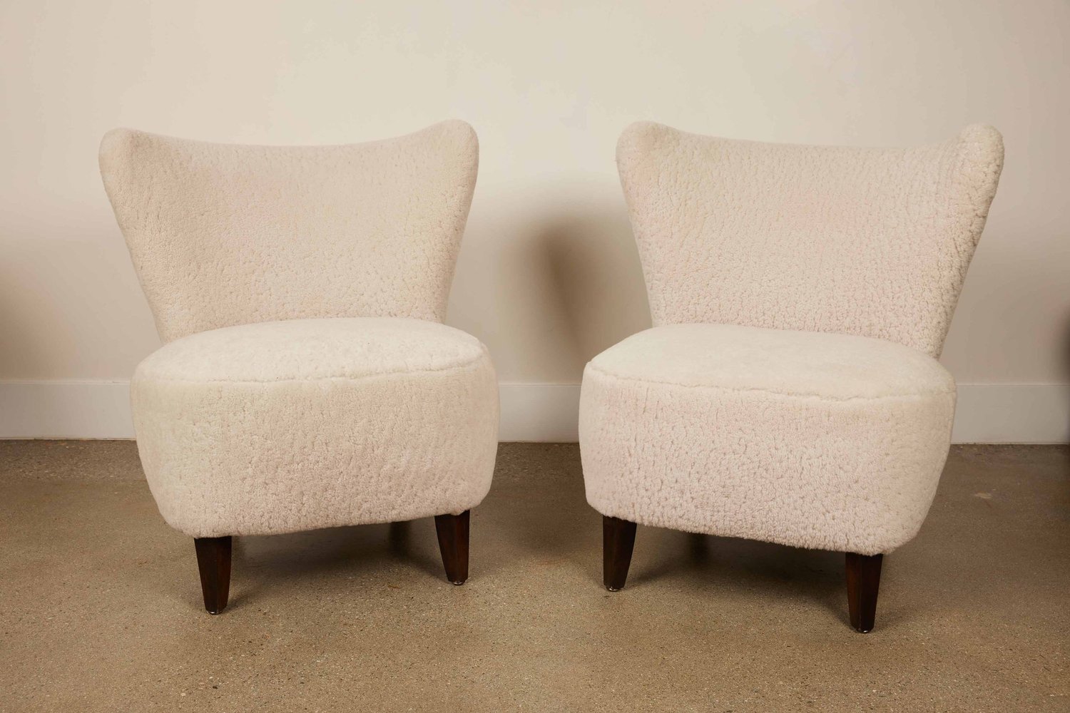 Pair of vintage mid-century modern armless lounge chairs upholstered in cream bouclé fabric with wood legs.