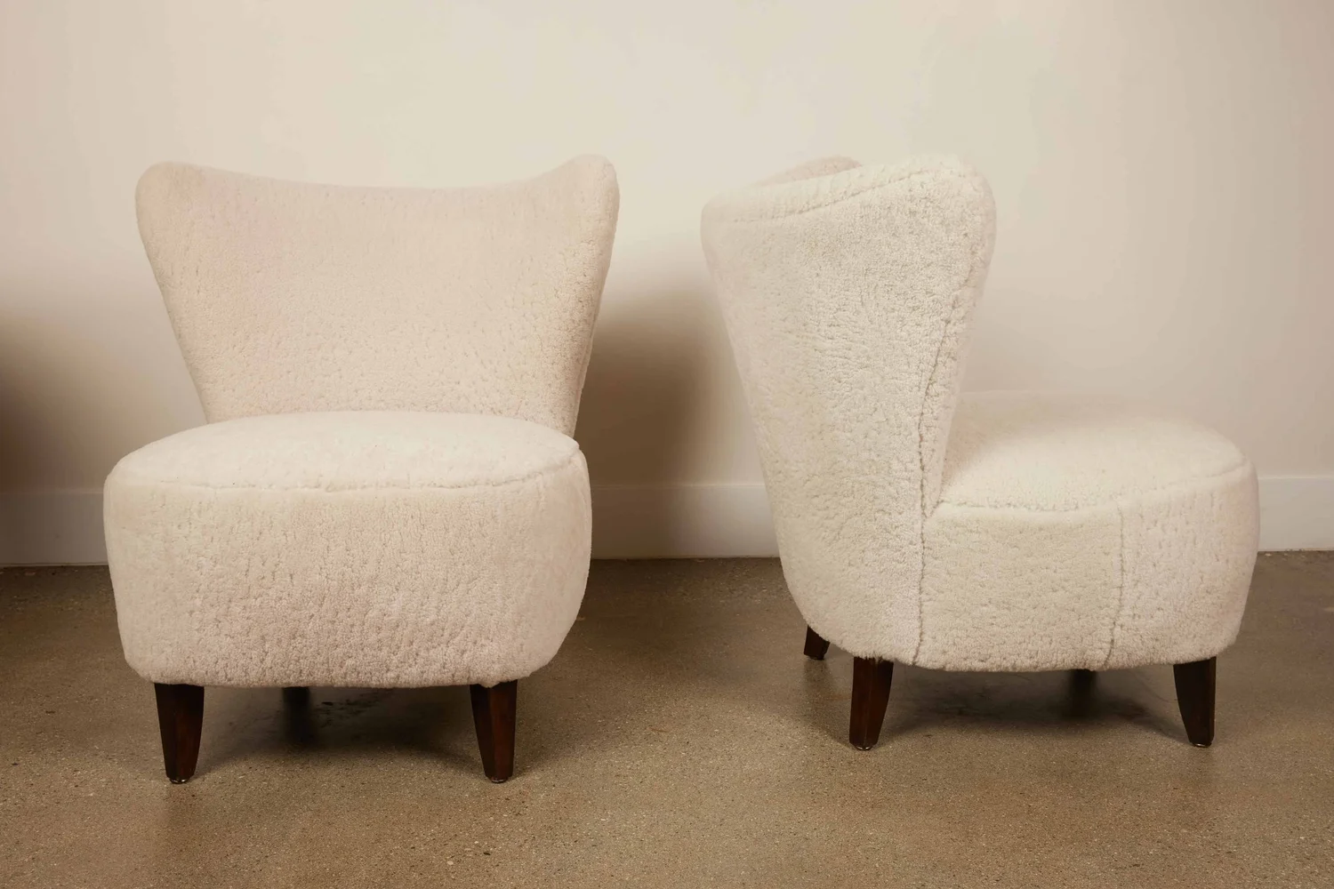 Pair of vintage mid-century modern slipper chairs upholstered in white bouclé fabric with dark wood legs.