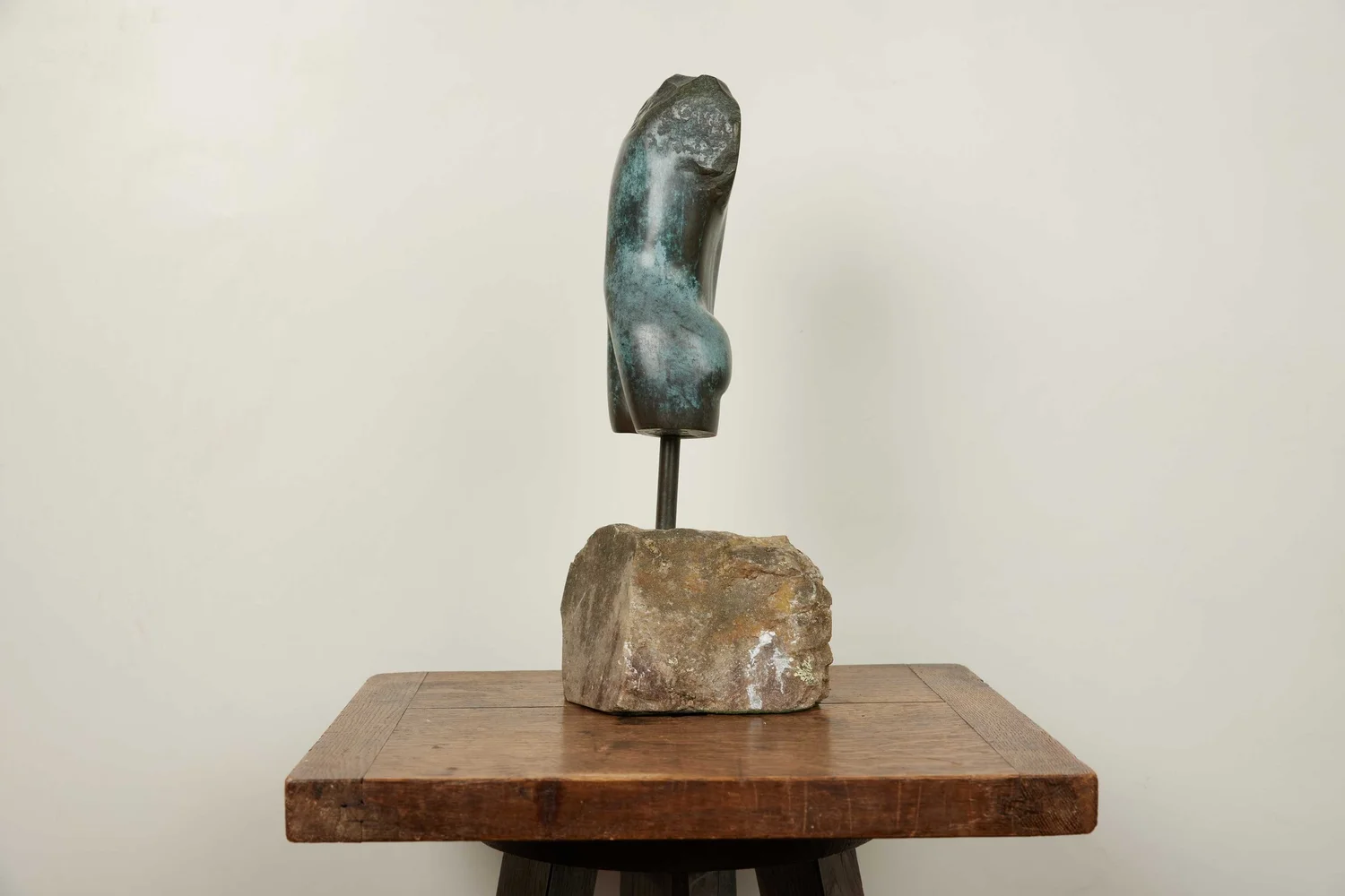 Vintage bronze torso sculpture mounted on a rough stone base, displayed on a rustic wooden table.