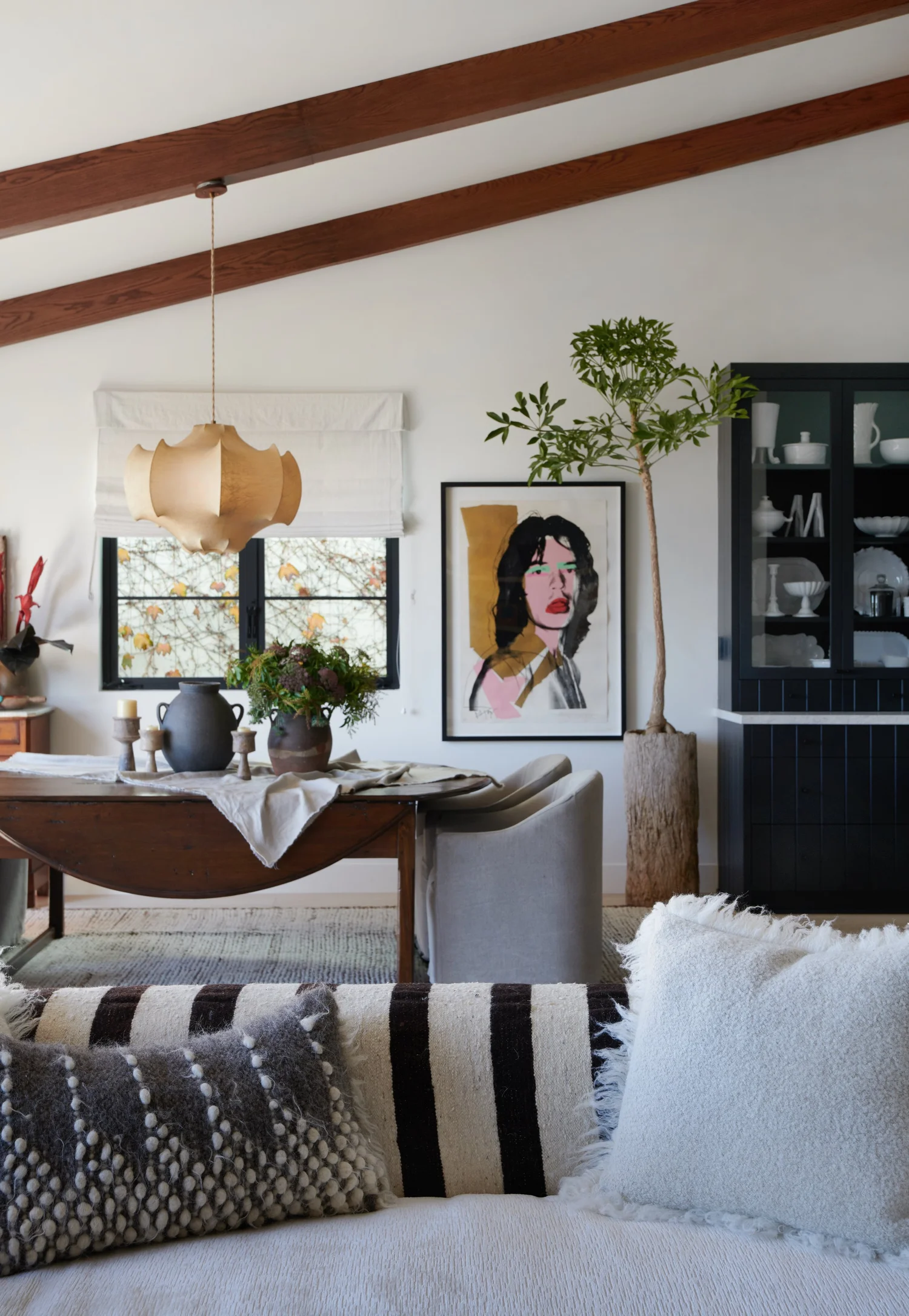 Warm modern dining room with wood beams, vintage drop-leaf table, contemporary art, and textured sofa.