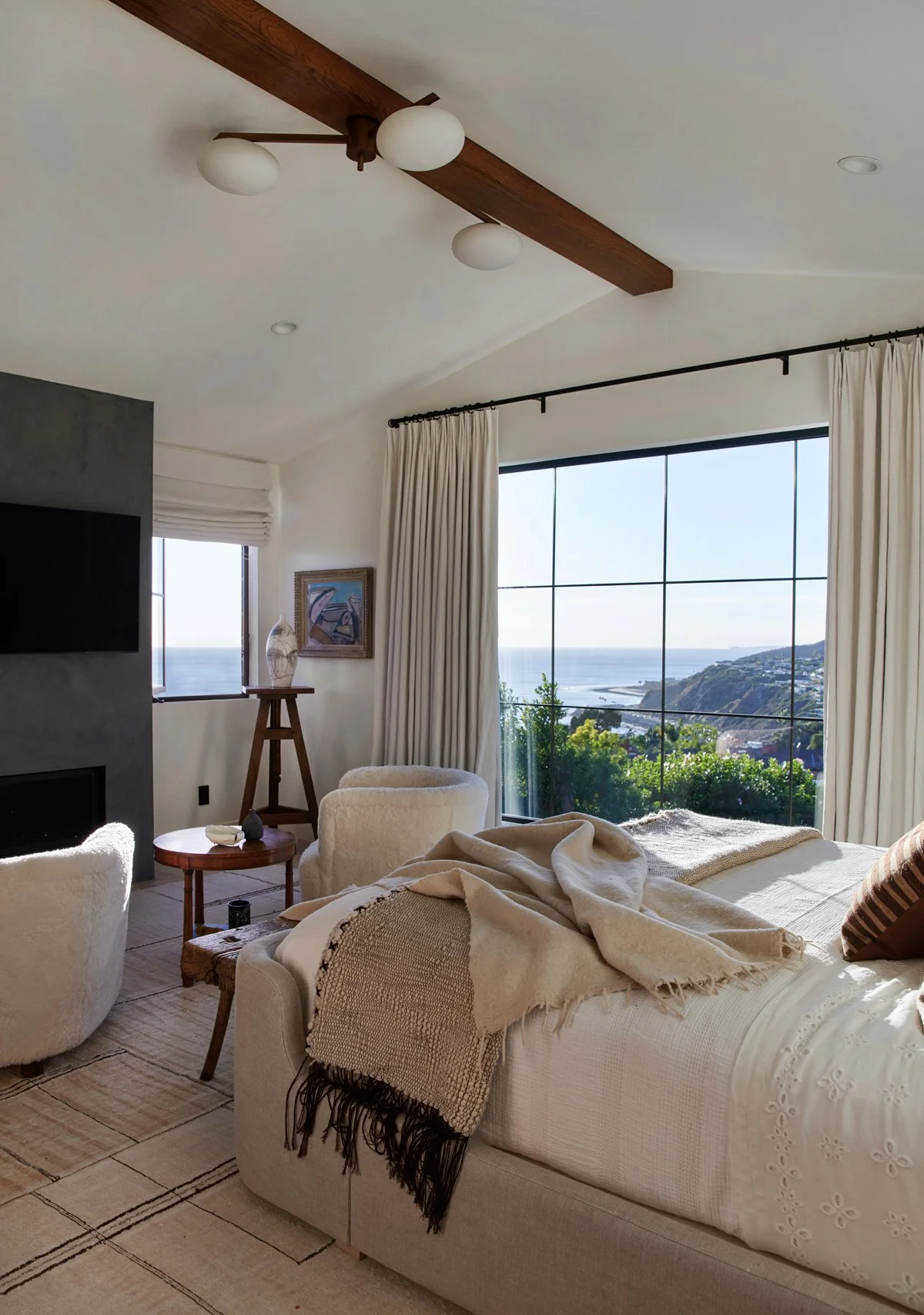 Warm modern bedroom with ocean views, exposed wood beam, and textured neutral bedding.