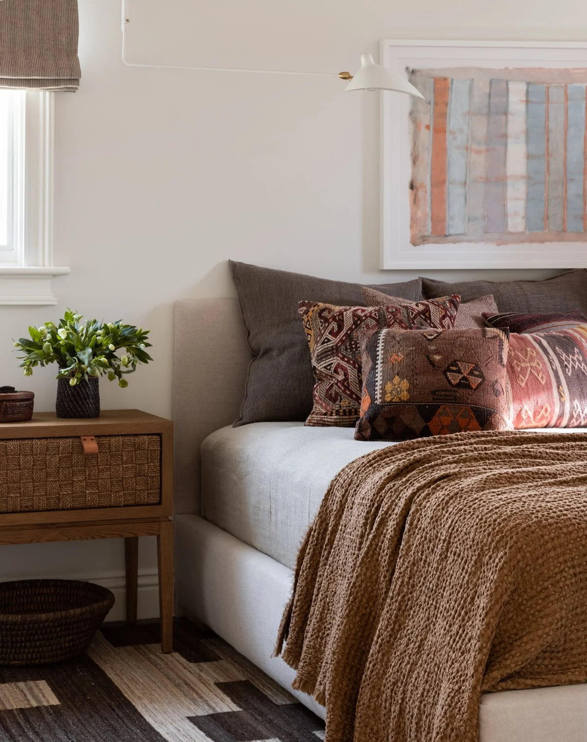 Warm modern bedroom with vintage kilim pillows, textured brown throw, and woven wood nightstand.