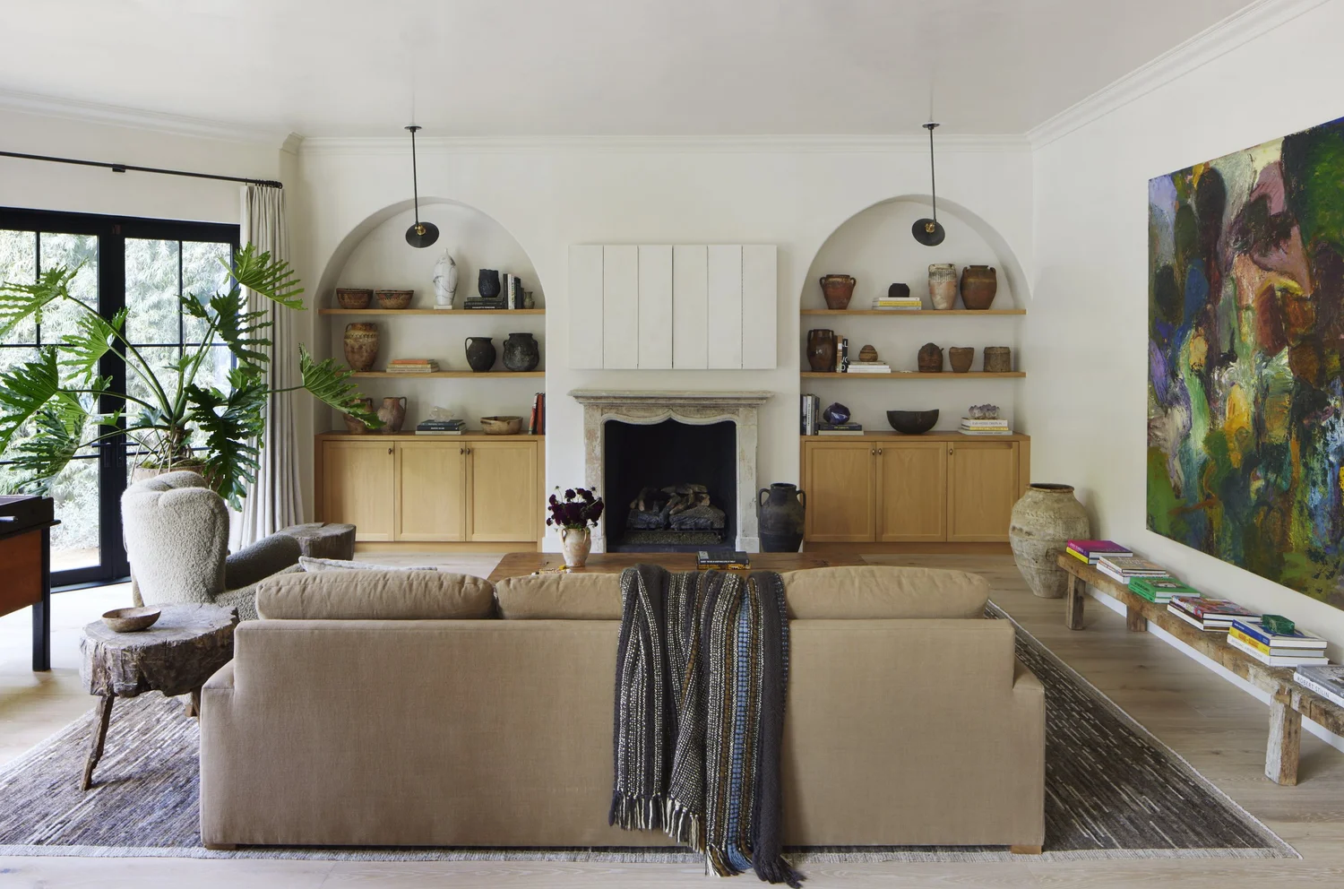 Warm modern living room with arched built-ins, vintage pottery, a beige sofa, and large abstract painting.