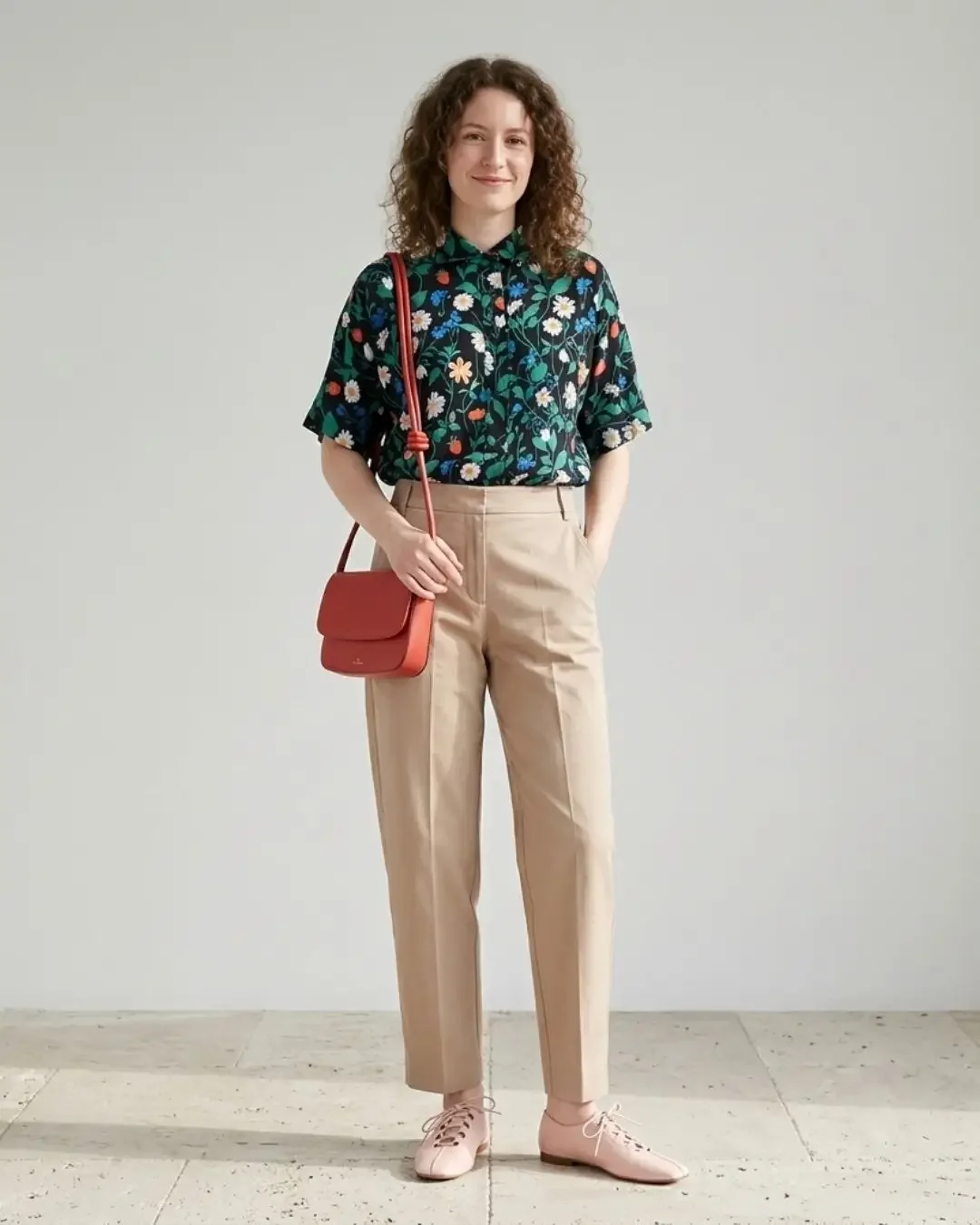 Spring outfit idea — navy floral shirt, camel tapered trousers, coral crossbody bag and pink lace-up flats for a statement-print-on-warm-neutral look