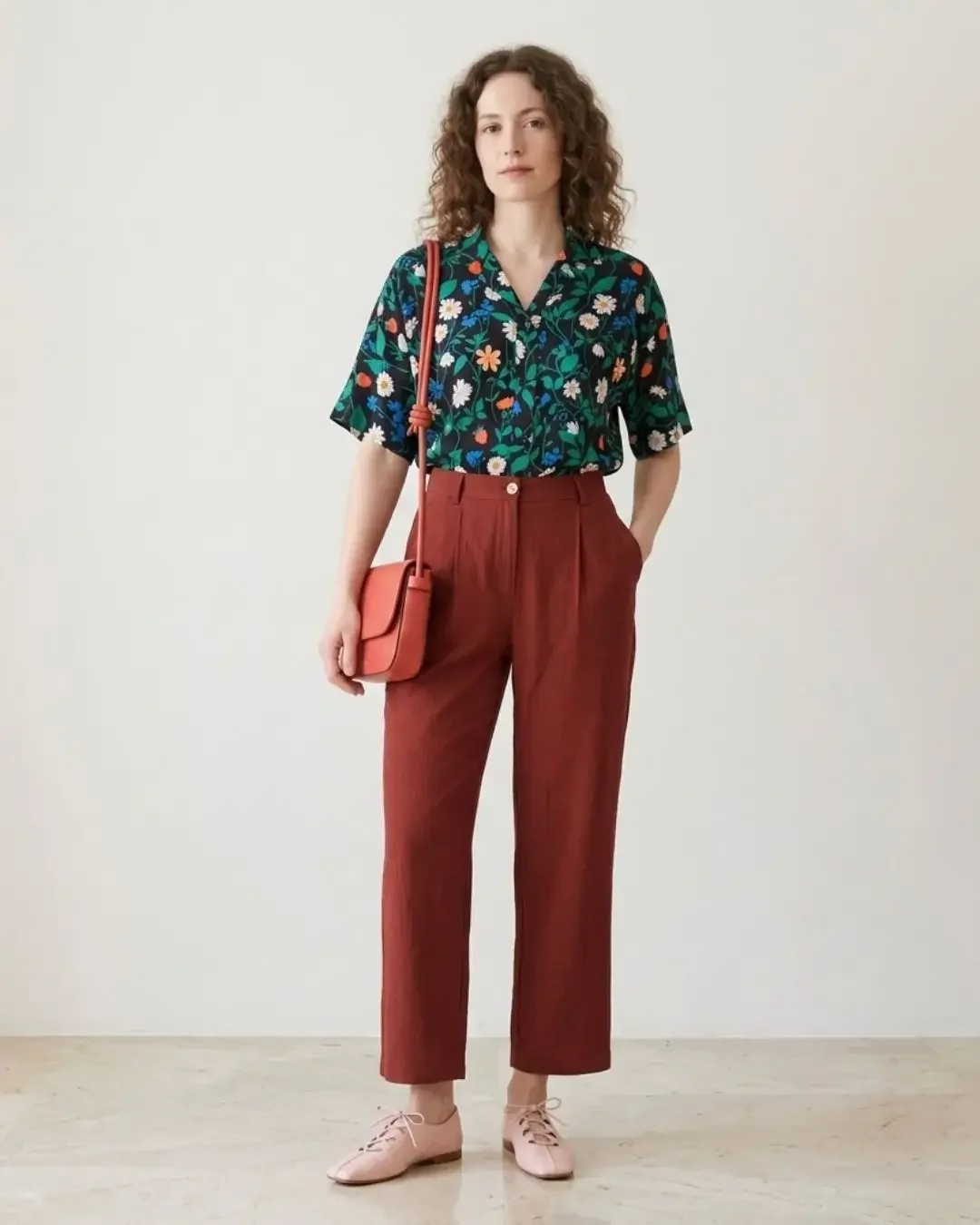 Spring outfit idea — navy floral shirt with green leaves, burgundy trousers, coral crossbody bag and pink flats for a print-on-solid warm palette.