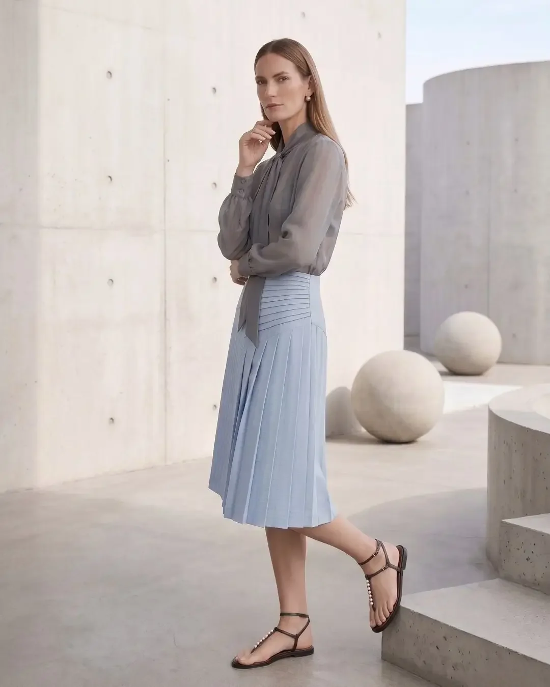 Side view of sheer grey blouse and pleated blue midi skirt with architectural spheres — Wonder Wardrobe spring capsule wardrobe 2026.