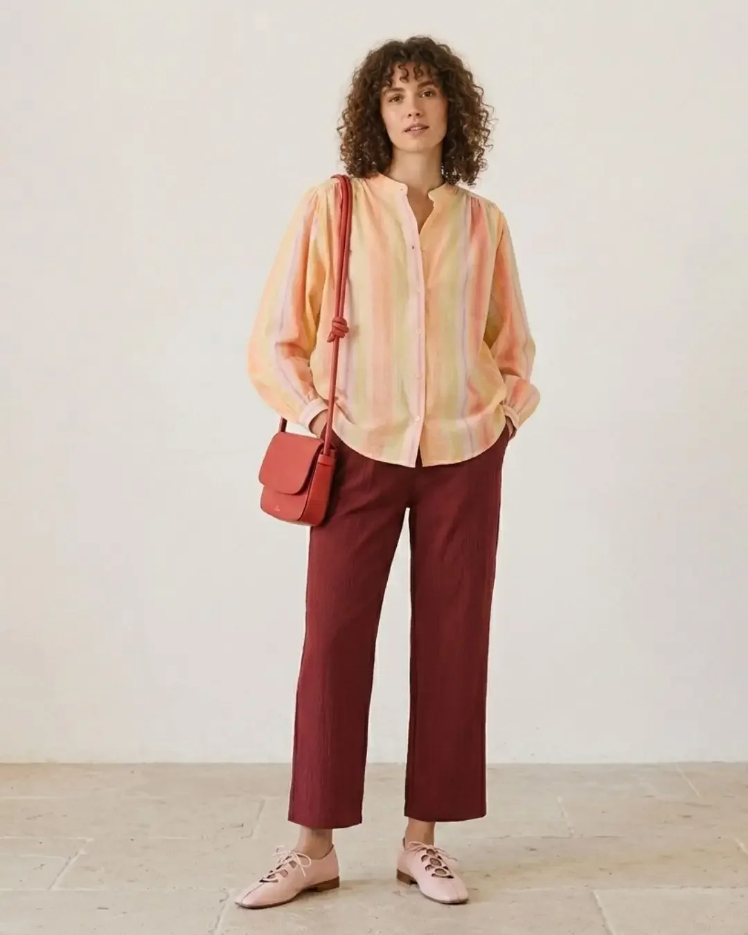 Spring outfit idea — warm-gradient striped blouse, burgundy trousers, coral crossbody bag and pink lace-up flats in a tonal warm-on-warm palette