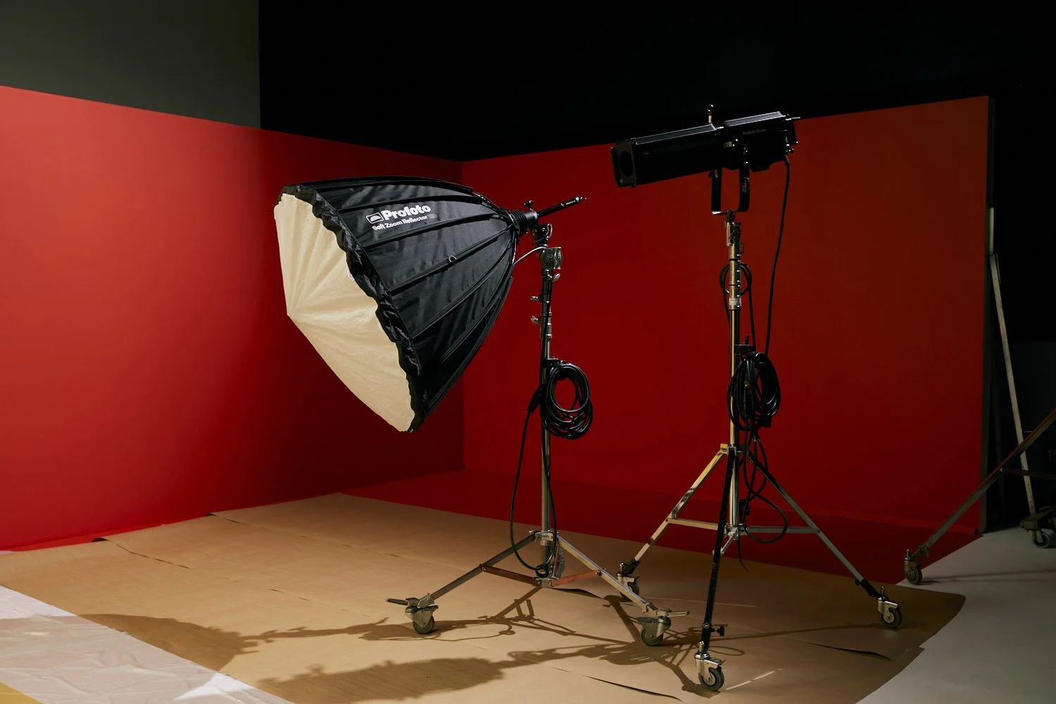Photography studio setup with red backdrop, softbox lighting, and camera equipment on stands.