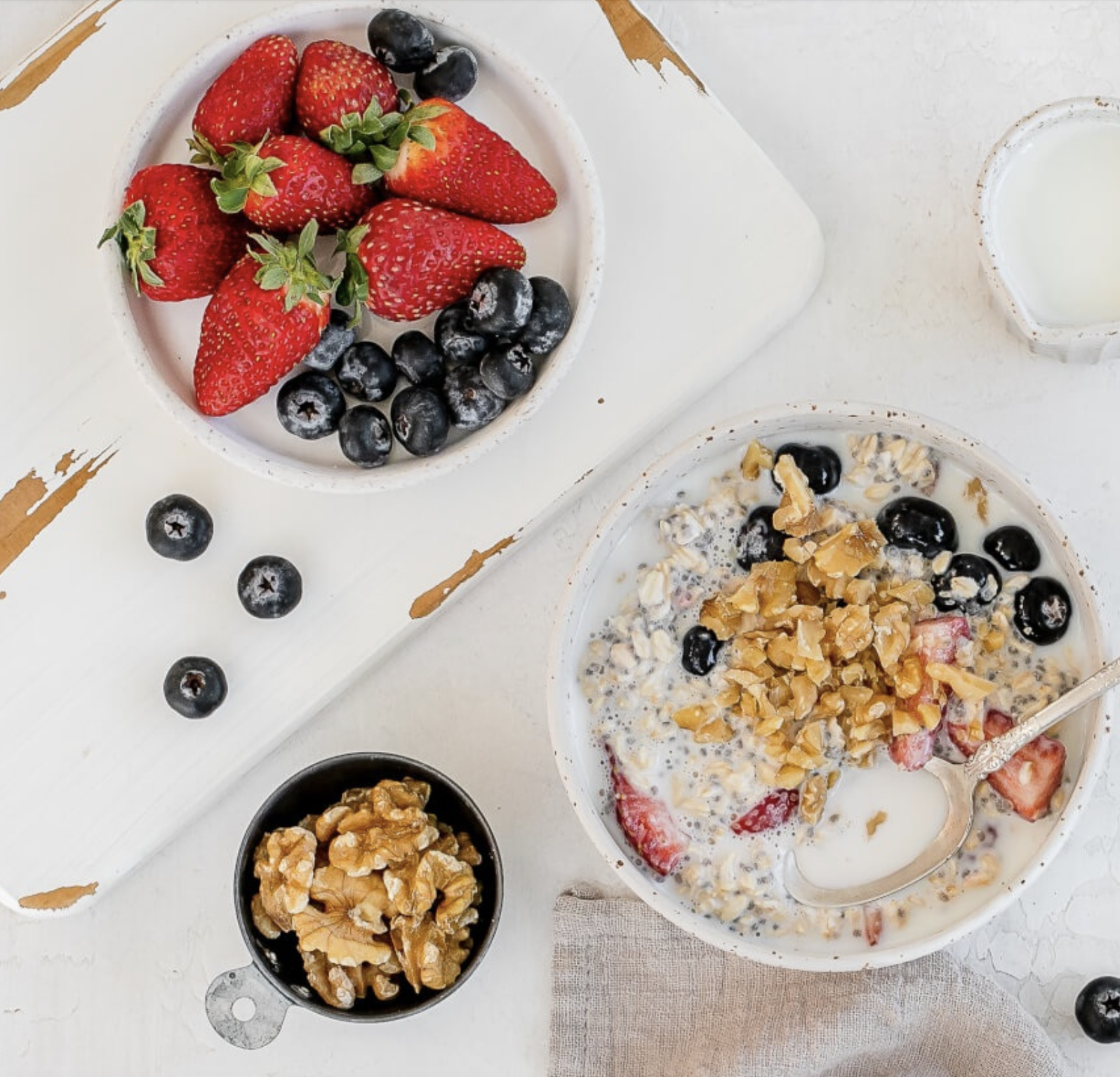 A bowl of berries, a bowl of walnuts and a breakfast bowl of overnight oats