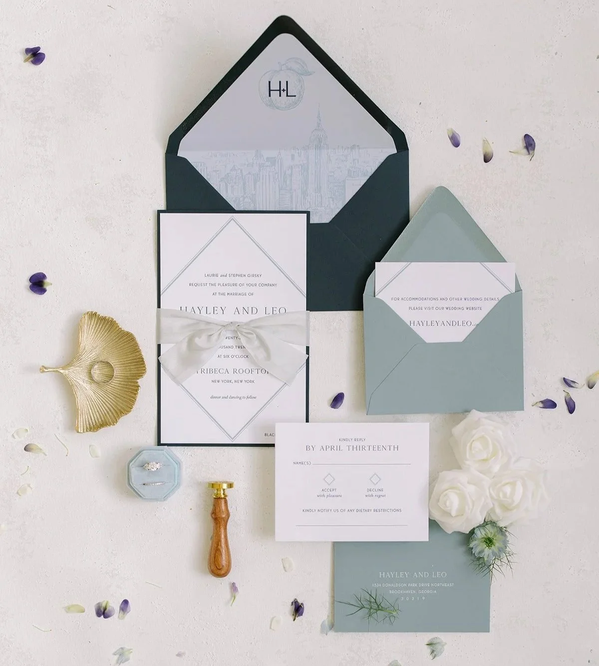 Custom invitation suite in shades of blue with a diamond design and silk ribbon. Letterpress printed. On a cream background surrounded by flower petals.