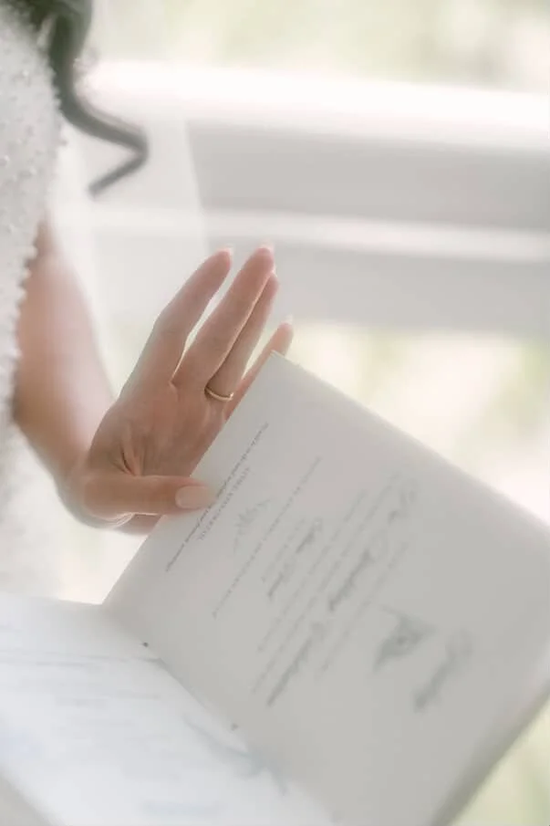 Image of a book wedding invitation open to an itinerary page held by the bride.