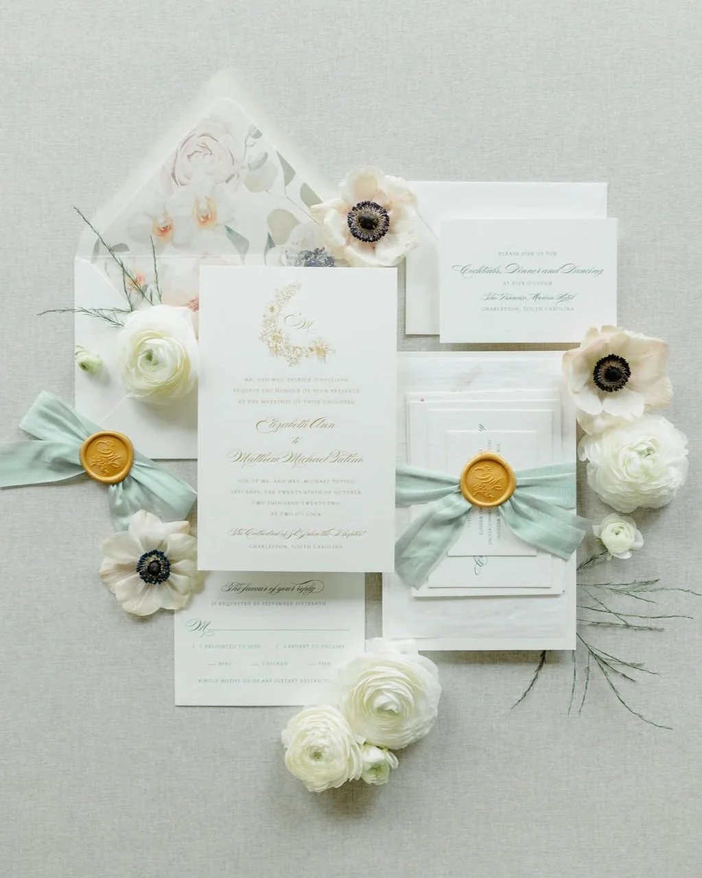 Gold engraved wedding inviation for a Charlestcon, SC wedding. With a gold wax seal, sage silk ribbon, and watercolor floral envelope liner. Surrounded by white anemones and ranunculus on a soft, beige background.