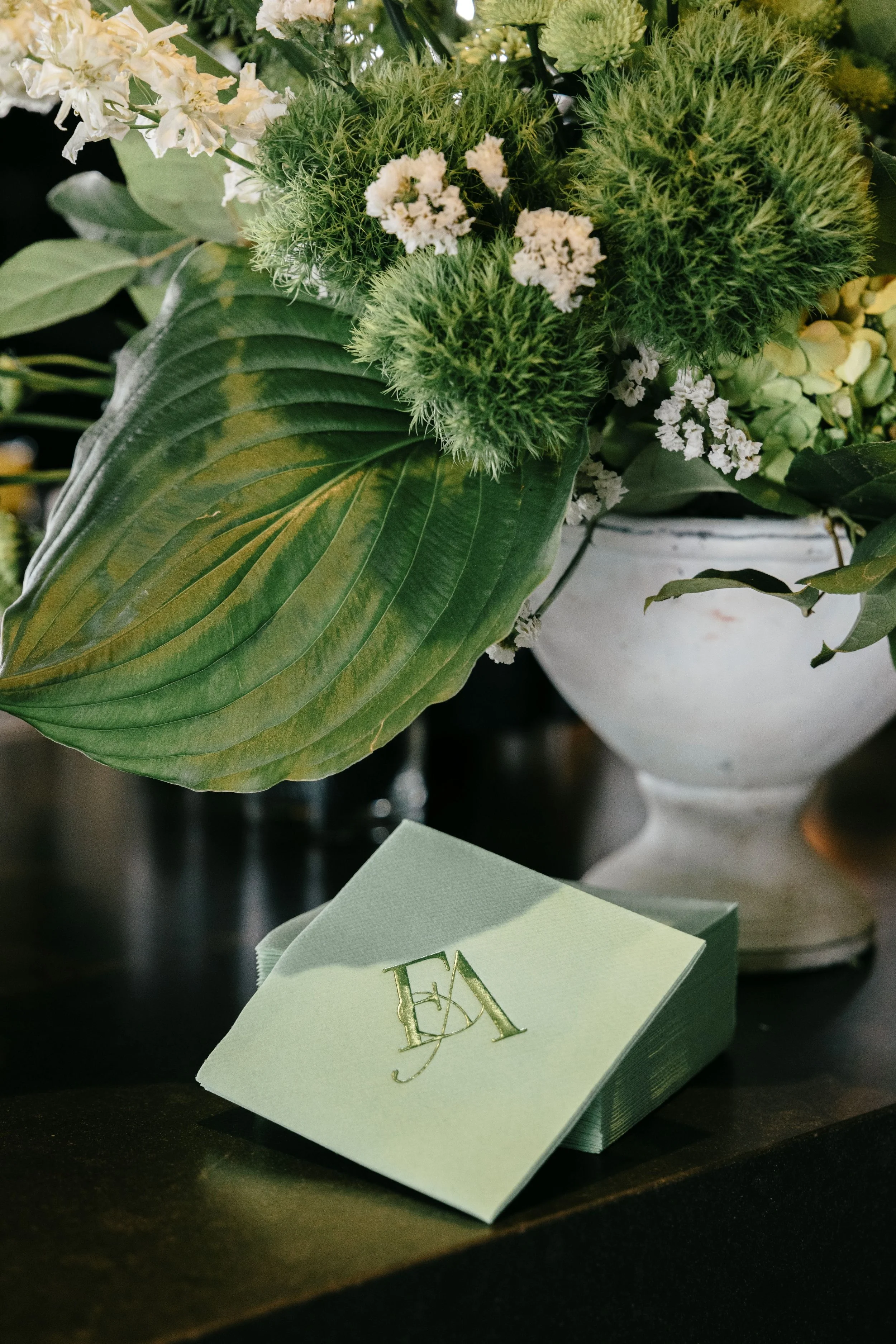 A green monogram on a green cocktail napkin by a gorgeous floral display for a wedding at the Ivy at Ellis Preserve