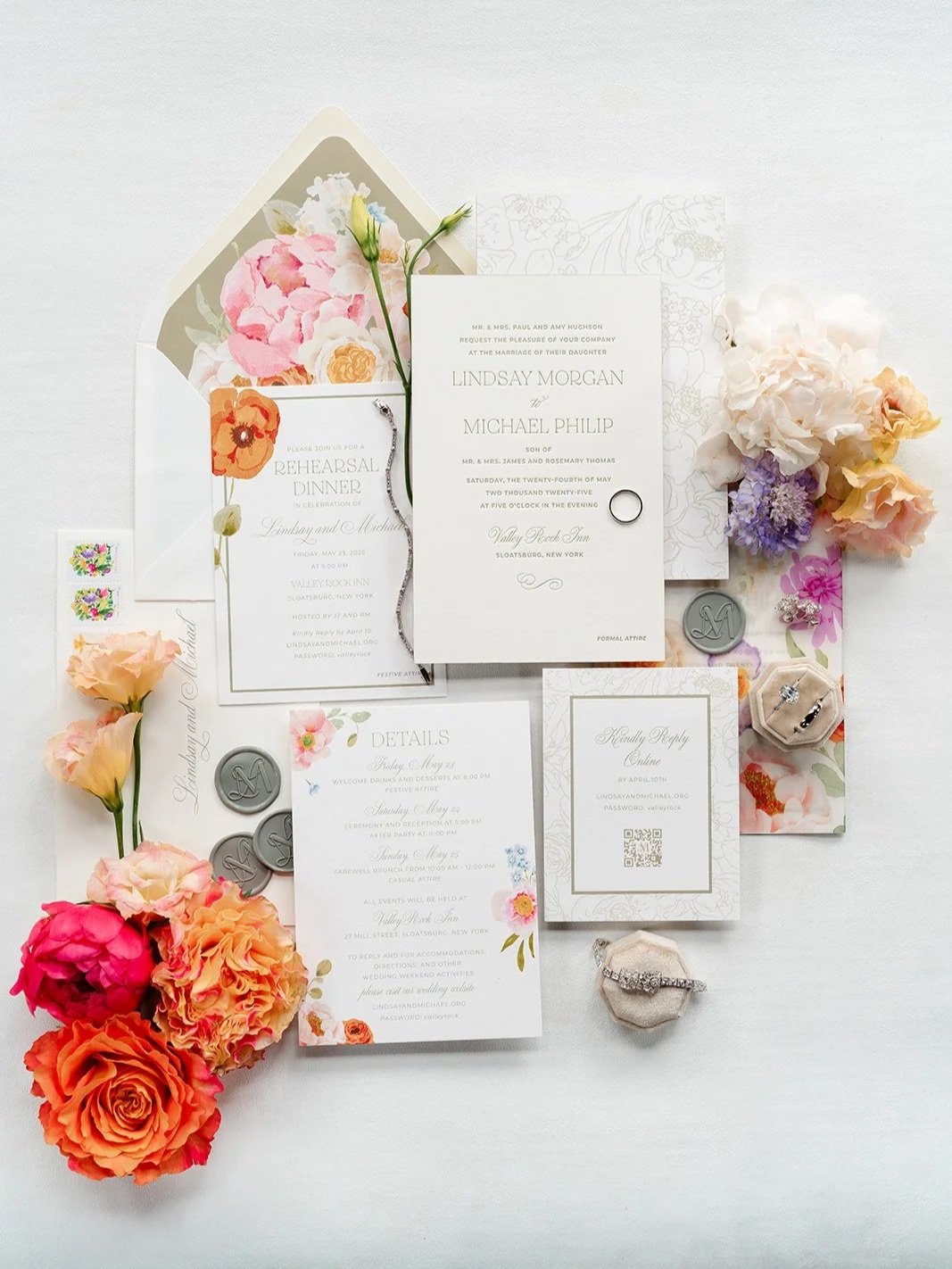 flat lay of custom designed wedding invitations with sage green letterpress print, sage green wax seals, a beautiful green envelope liner with watercolor floral elements surrounded by vibrant and pastel flowers.