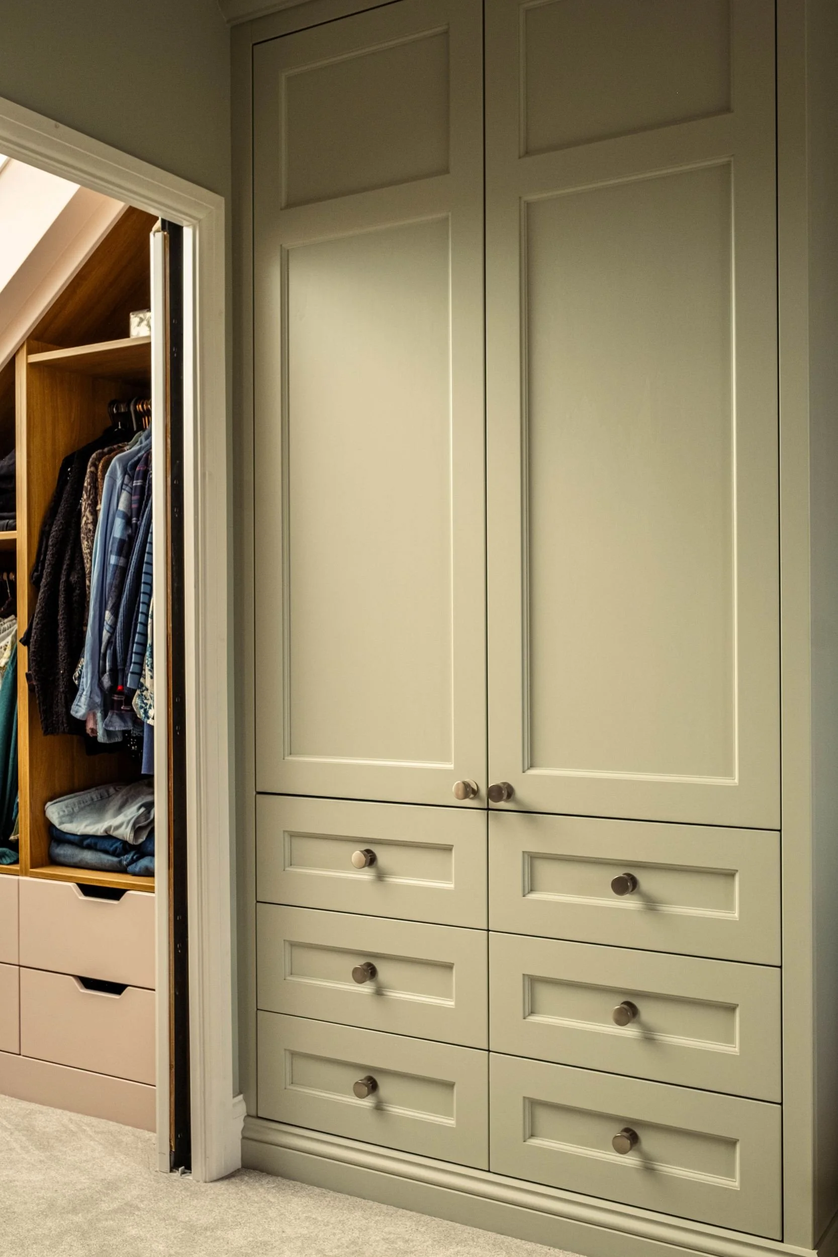 A made to measure fitted wardrobe with two Shaker style doors and six Shaker style doors. The wardrobe is painted green and to the left there is a walk in wardrobe with open shelving and hanging rail space and drawers.