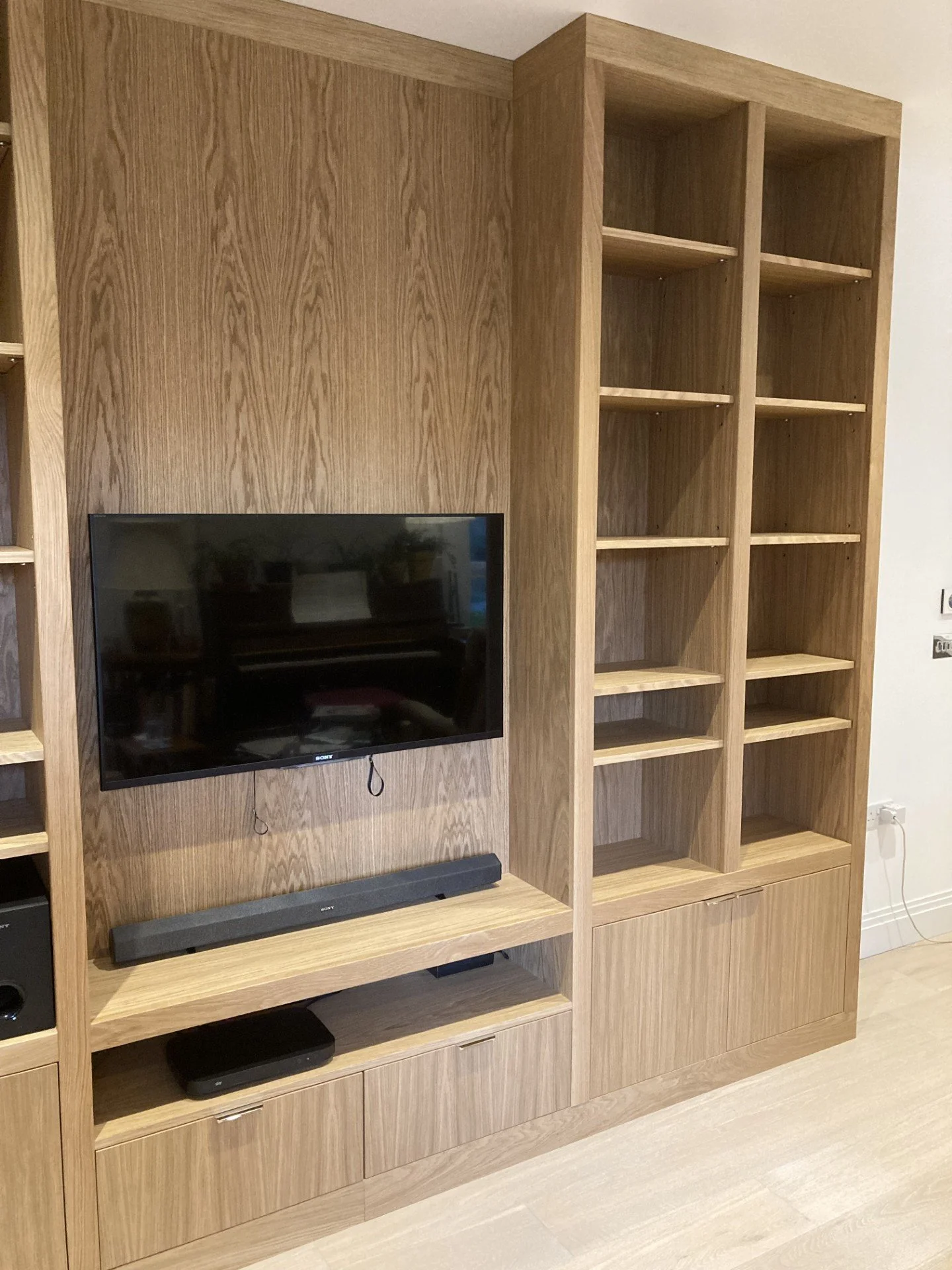Close up of a made to measure bespoke media unit made from oak veneered boards and solid oak. Media unit consists of cupboards, adjustable shelving and a space where the TV is mounted.